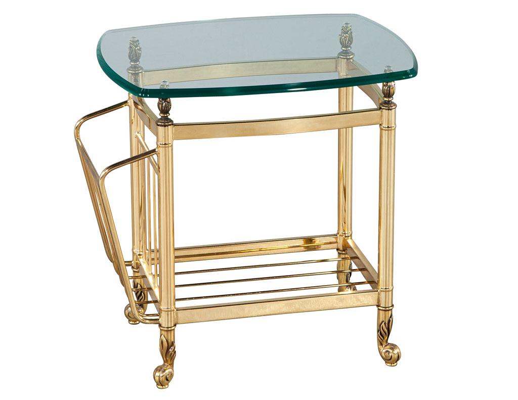 Vintage brass magazine stand end table. Beautiful brass table with unique sculpted accents on top and feet. Angled magazine compartment with lower underside storage. Completed with a thick curved edge glass top. Glass top all original in good