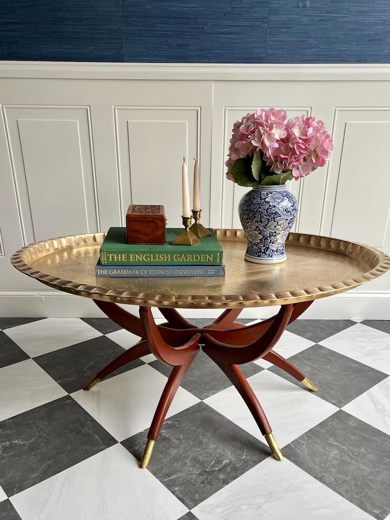 A true conversation piece, this vintage folding coffee table marries elegance and practicality in one collectible silhouette. Featuring a scalloped solid brass tray with intricate hand-etched detailing, it brings a warm, ornamental glow to any