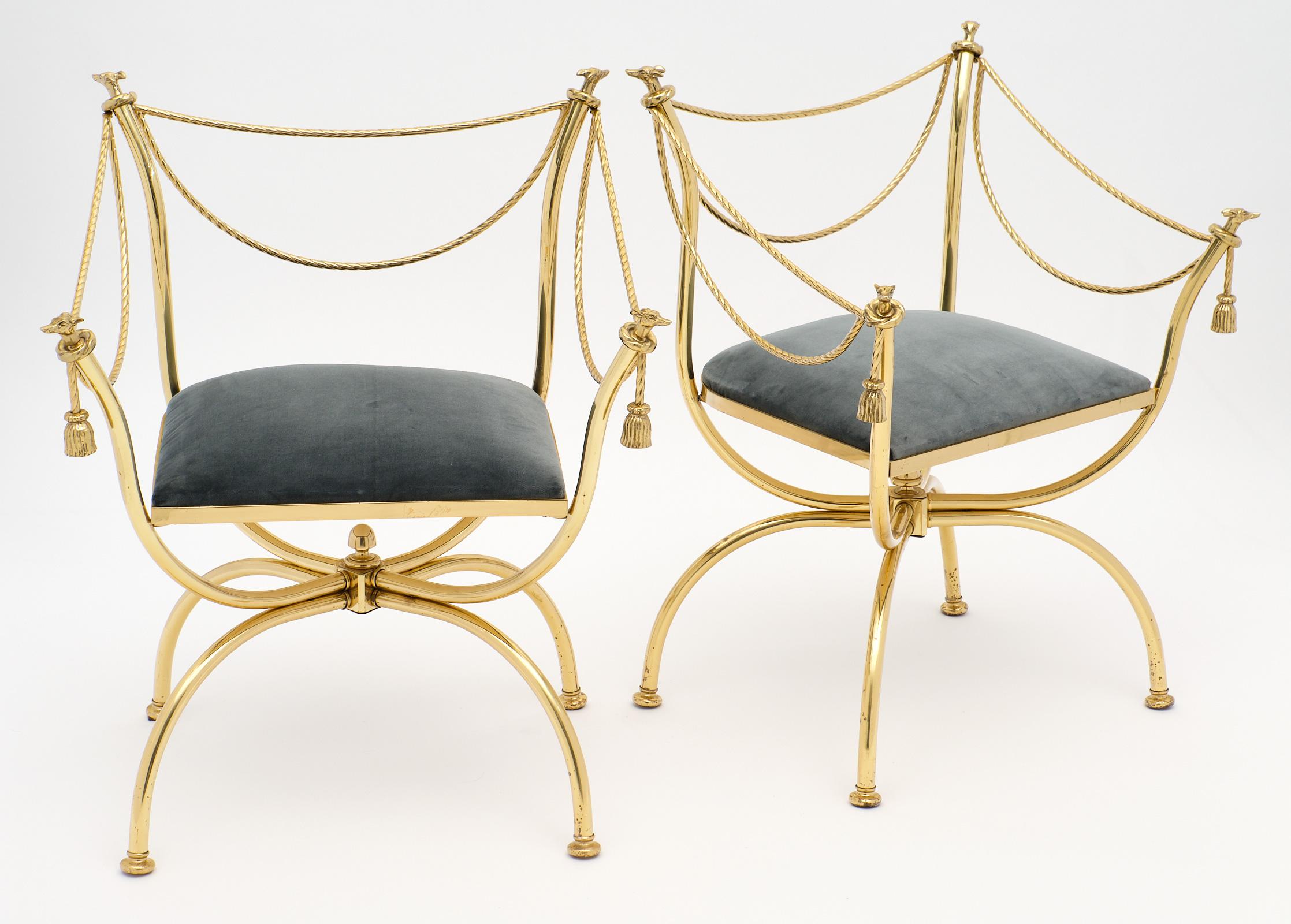 An iconic pair of sold gilt brass armchairs by Maison Charles. The finest cast quality is displayed in the greyhound finials, ropes, and tassels. They have been newly professionally upholstered in a dark gray velvet.