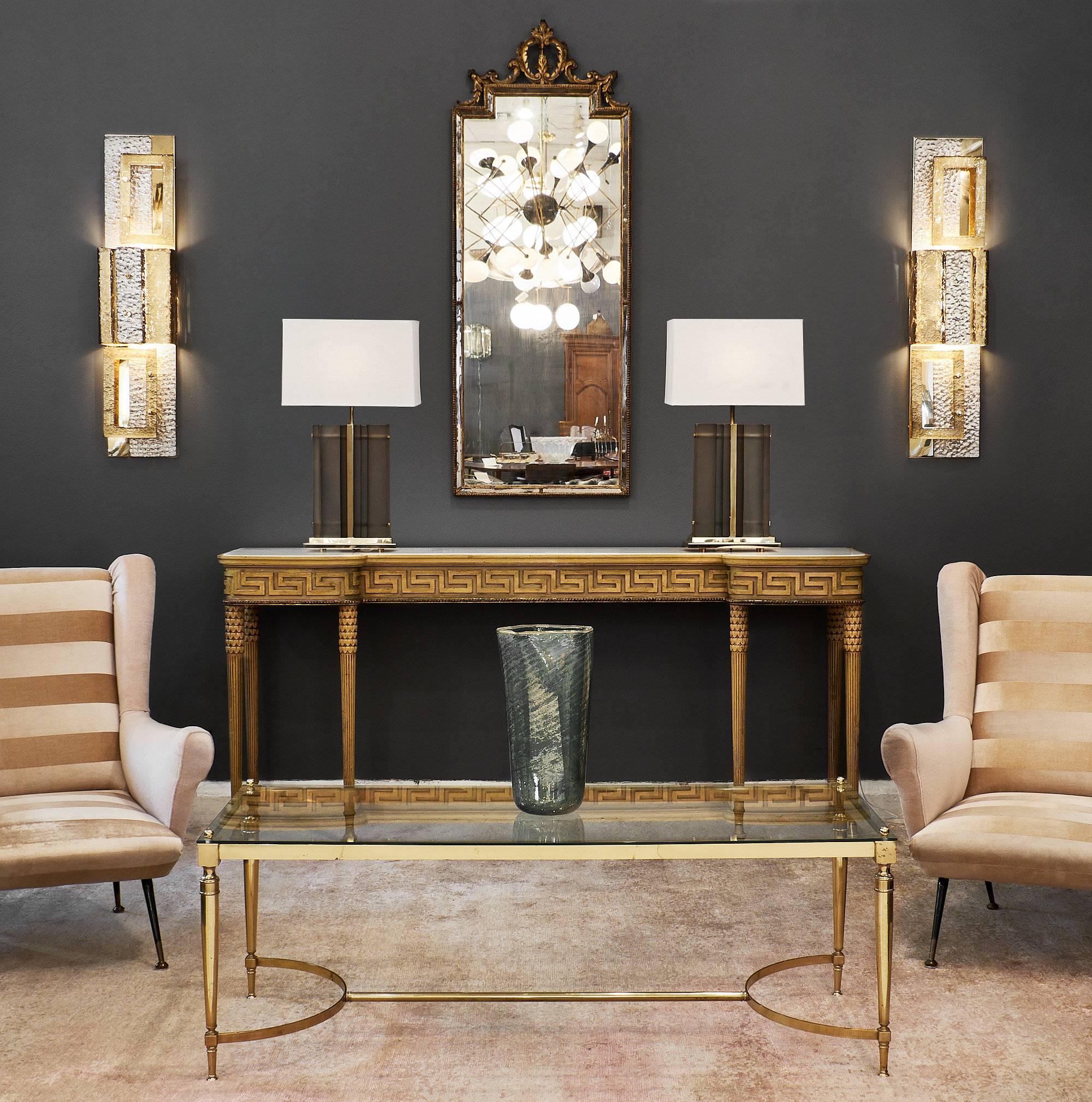 French midcentury vintage brass coffee table in the style of Baguès. This piece is made of gilt brass featuring a clear glass top held by four finials. The four tapered legs are connected by a stretcher. This fine vintage table will fit beautifully