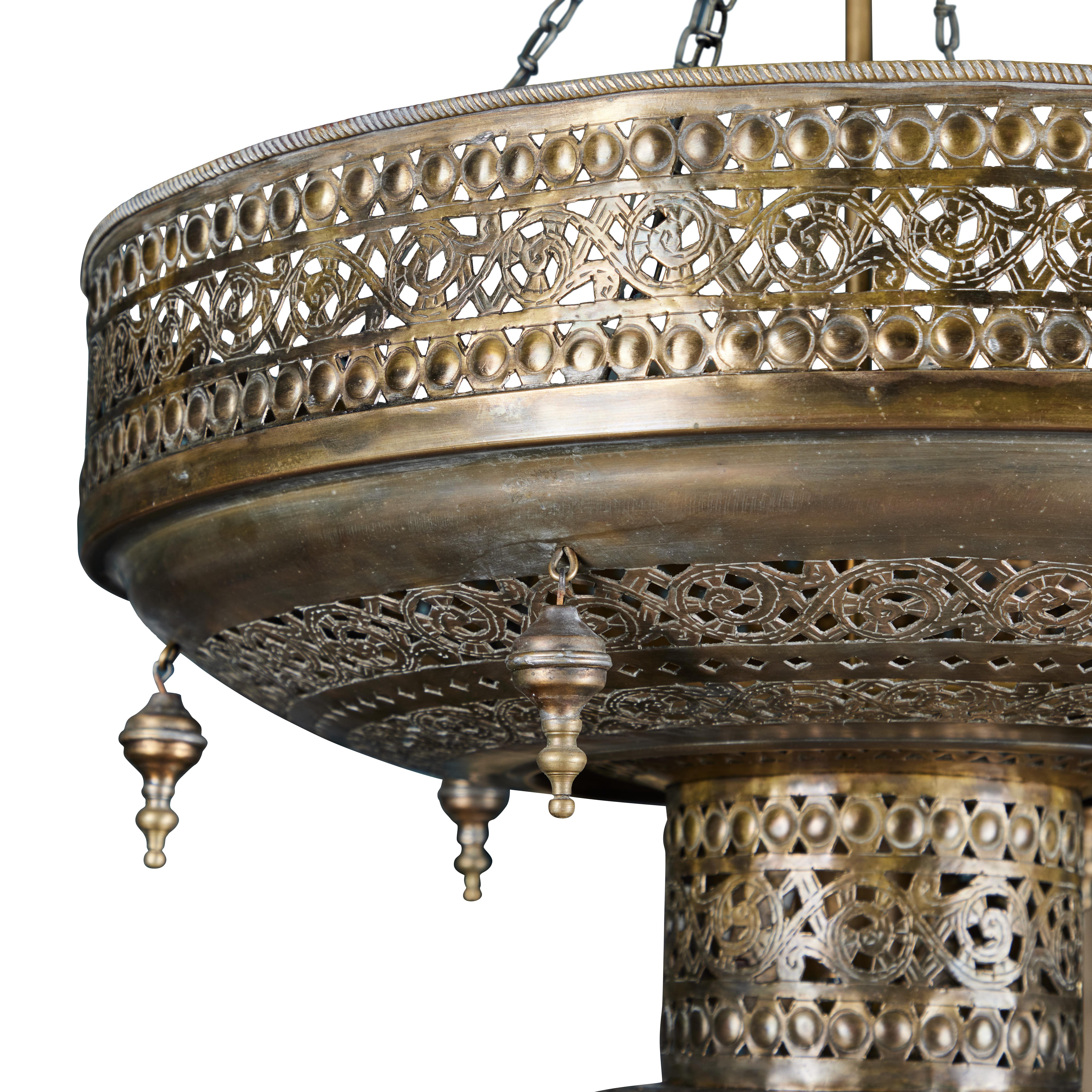 This exquisite 2-tier Moroccan light fixture is handcrafted and cut with fine delicate pierced panel designs and adorned with ornamental brass drops. It has a beautiful Moorish bronze patina finish and is a stunning piece of art as well as a