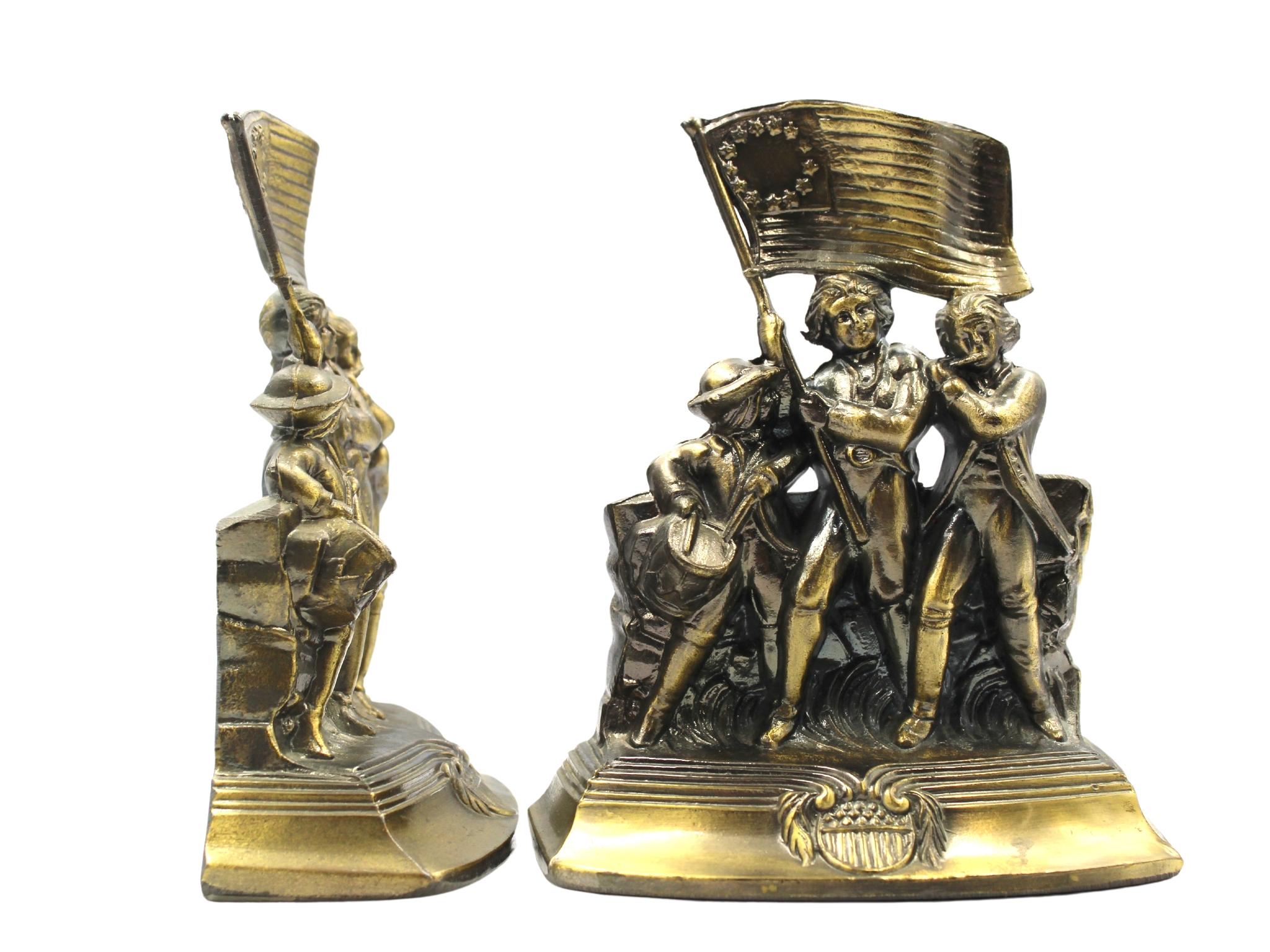 Offered is a set of vintage brass Revolutionary War soldiers bookends. Each bookend depicts a fife player, a drummer, and a flag bearer, marching in step together across a grassy field. The flag bearer hoists a large 13-star medallion flag into the
