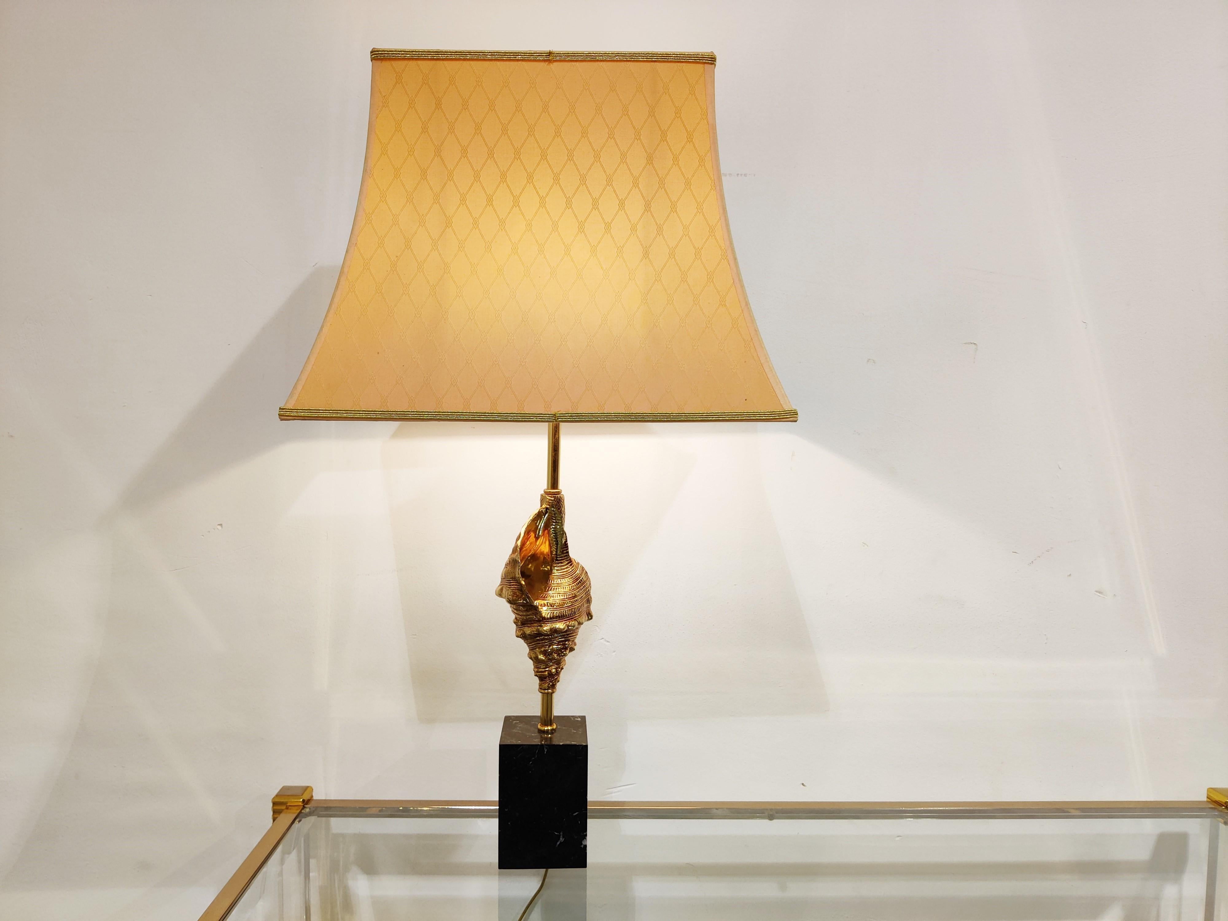 Beautiful brass snail sea shell table lamp in the style of Maison Charles.

This luxurious lamp has a brass and highly detailed shell center piece.

 Black marble base and the original lamp shade.

Good condition.

The lamp works with one