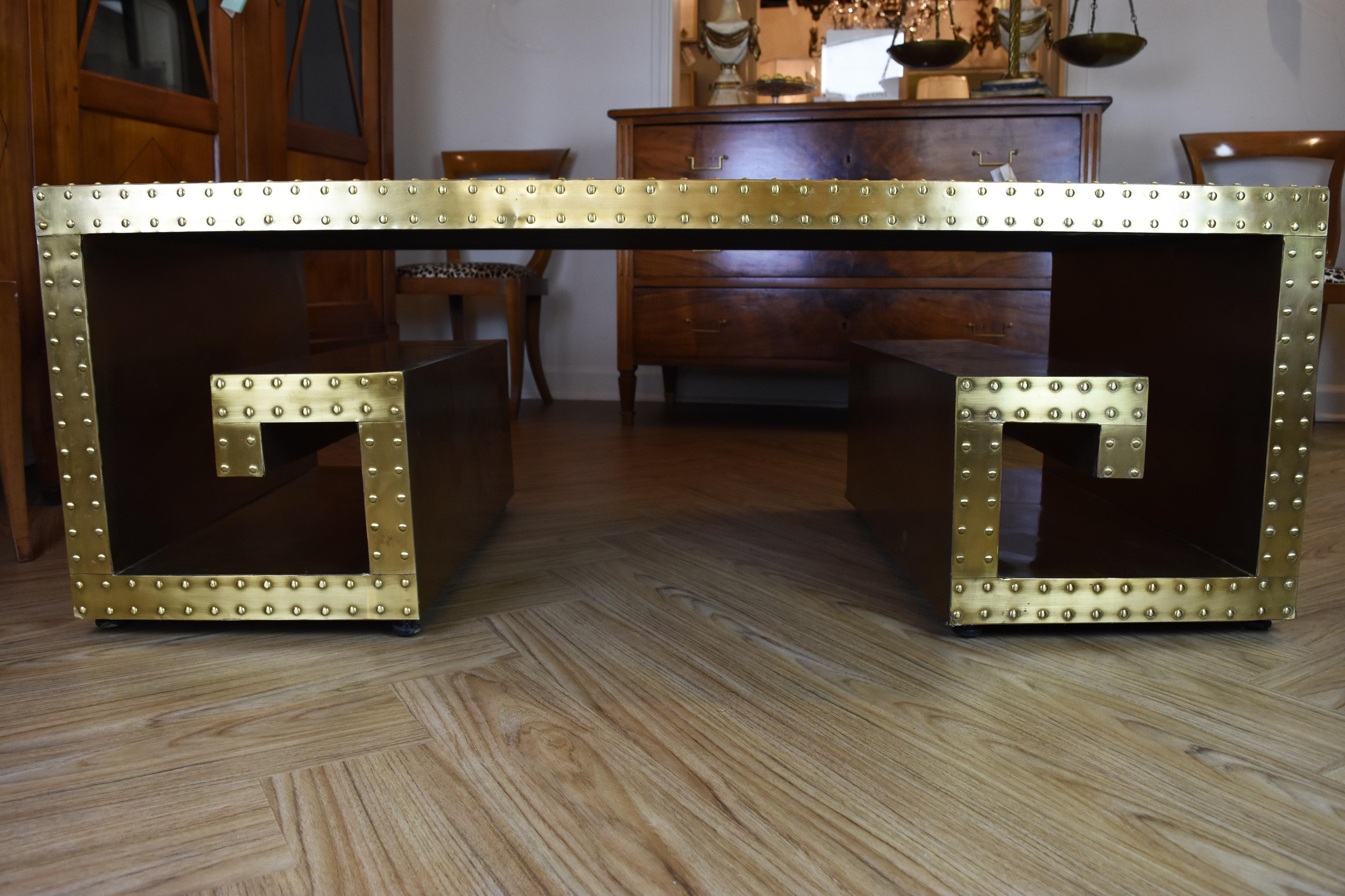 This vintage studded brass clad coffee table features a Greek key design. The top has several dents or imperfections but in no way diminishes the overall look of this striking piece.