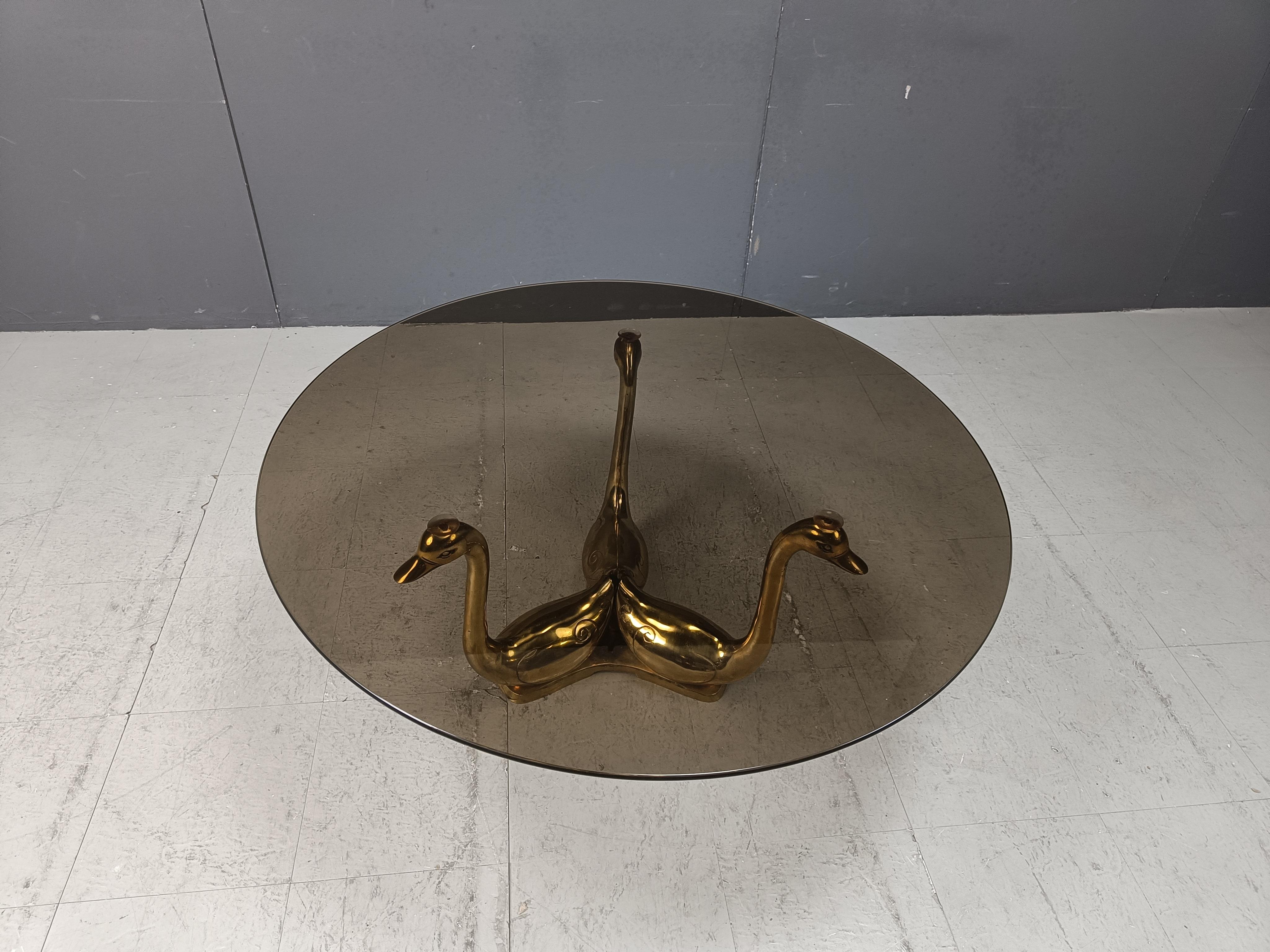 Hollywood regency brass swan coffee table.

The coffee table consists of a brass base featuring 3 brass swans and a round smoked glass top.

Diemensions:
Height: 47cm
Diameter: 105cm

Ref.: 64512112
