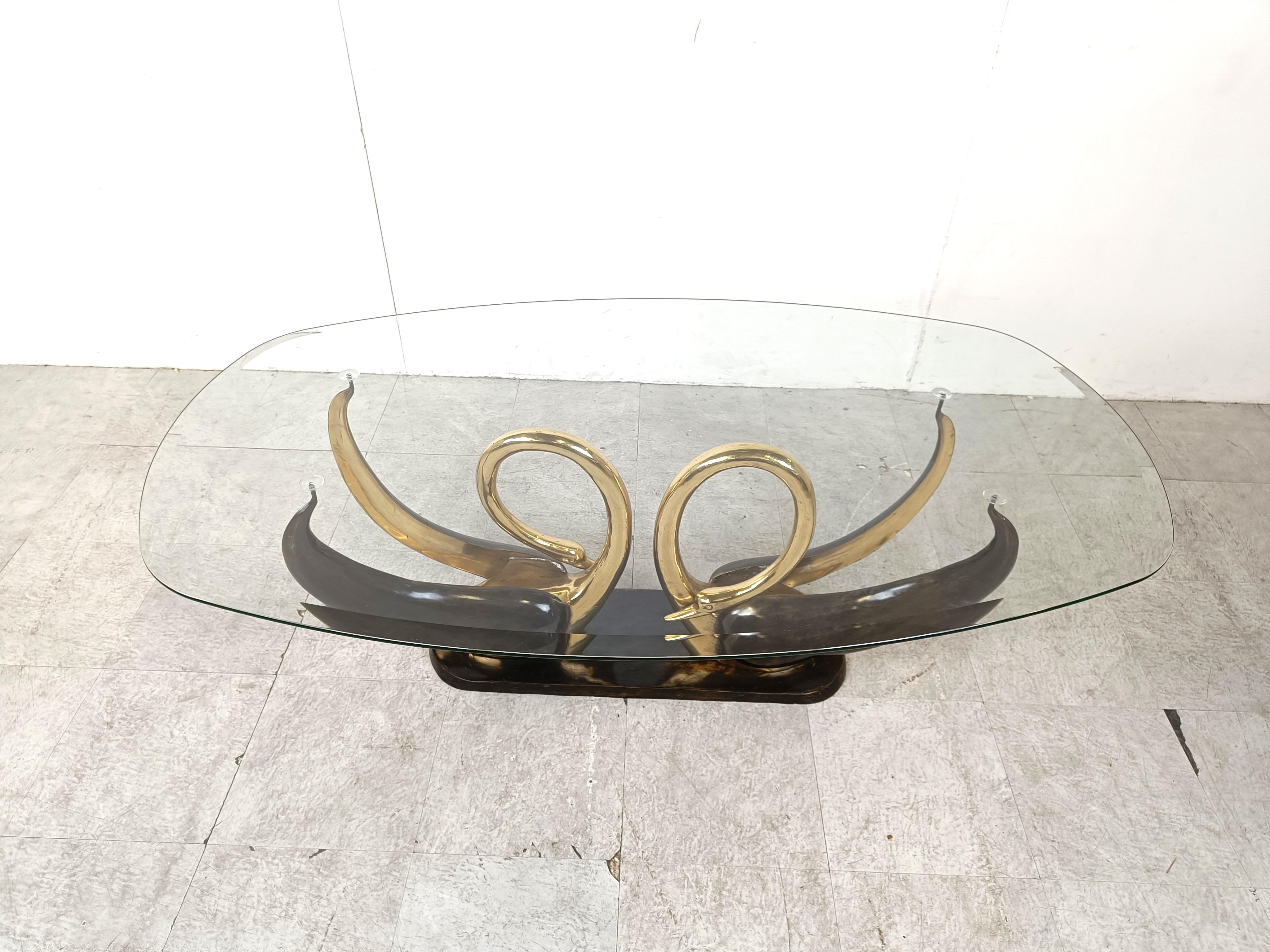 Elegant coffee table with a double swan base in brass with their curled necks.

Their wings serve as the table top supports.

The coffee table has an oval clear beveled glass top
​
This regency style coffee table surely is an eye catcher
​
Good