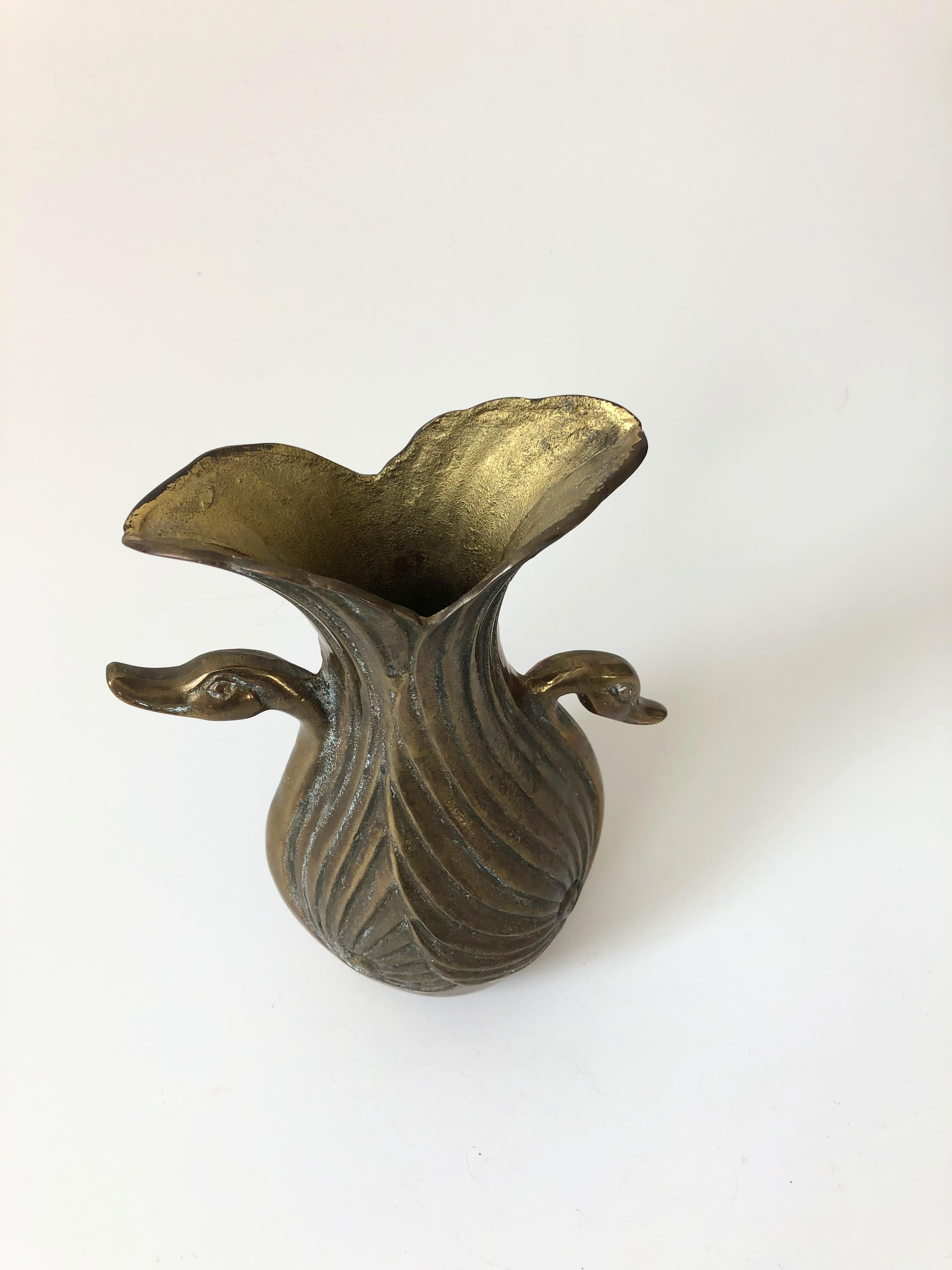 A vintage brass vase in the shape of a swan. Lovely Art Deco detailing featuring the heads of two swans on either side.
 