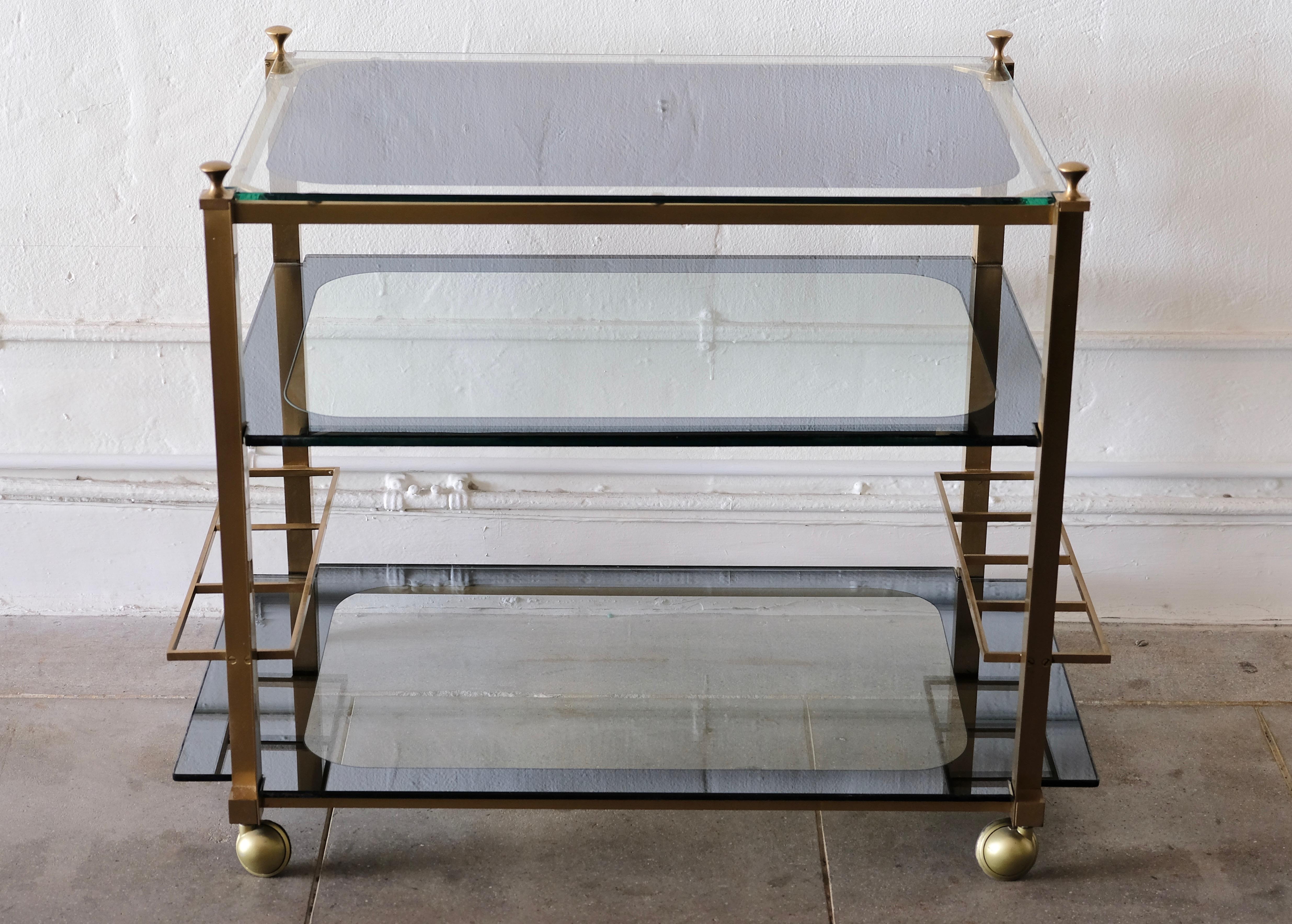 A beautiful vintage three tiered brass bar cart on its original brass casters. The cart has custom reverse painted mirrored glass. The top piece is mostly mirror with glass edge and the bottom two shelves are glass with mirror edge. There are two