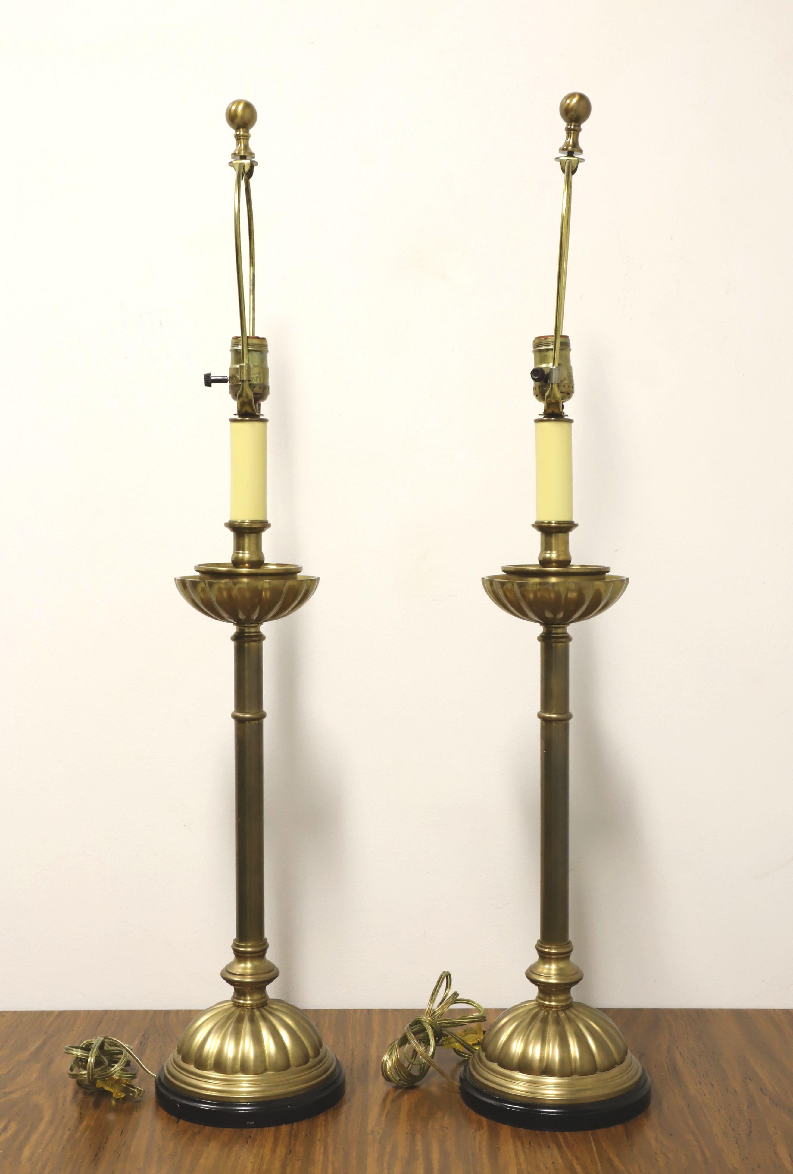 A pair of Traditional style candlestick table lamps, unbranded. Made of solid brass with a candlestick shape, a fluted upper tray at the base of the candle portion, white plastic supporting bulb socket to give an appearance of a candle, and a round