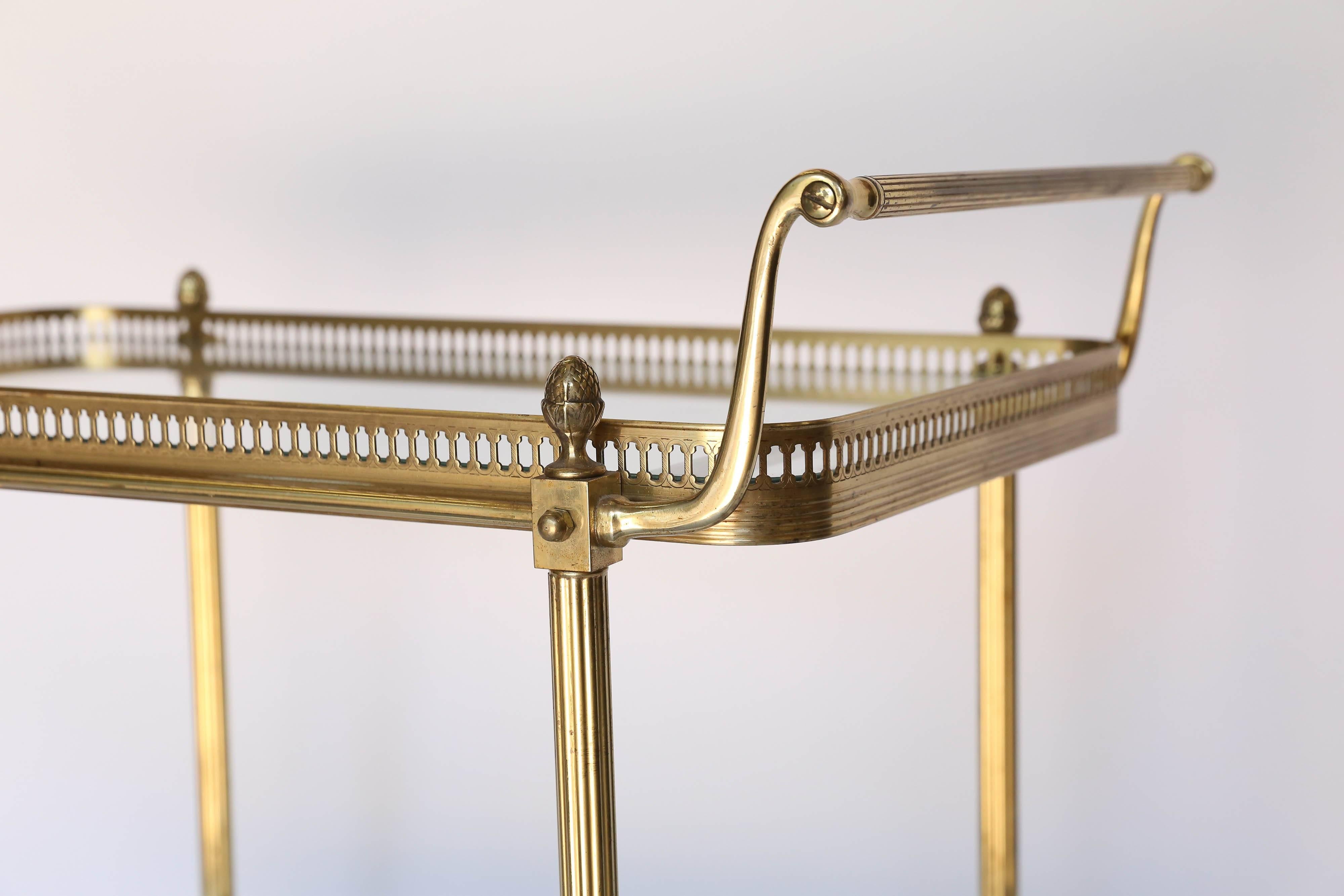 Vintage brass two-tier rolling bar cart constructed with two glass shelves and beautiful brass wheels for easy transport. Display your vintage glassware or serve your favorite cocktails and desserts.