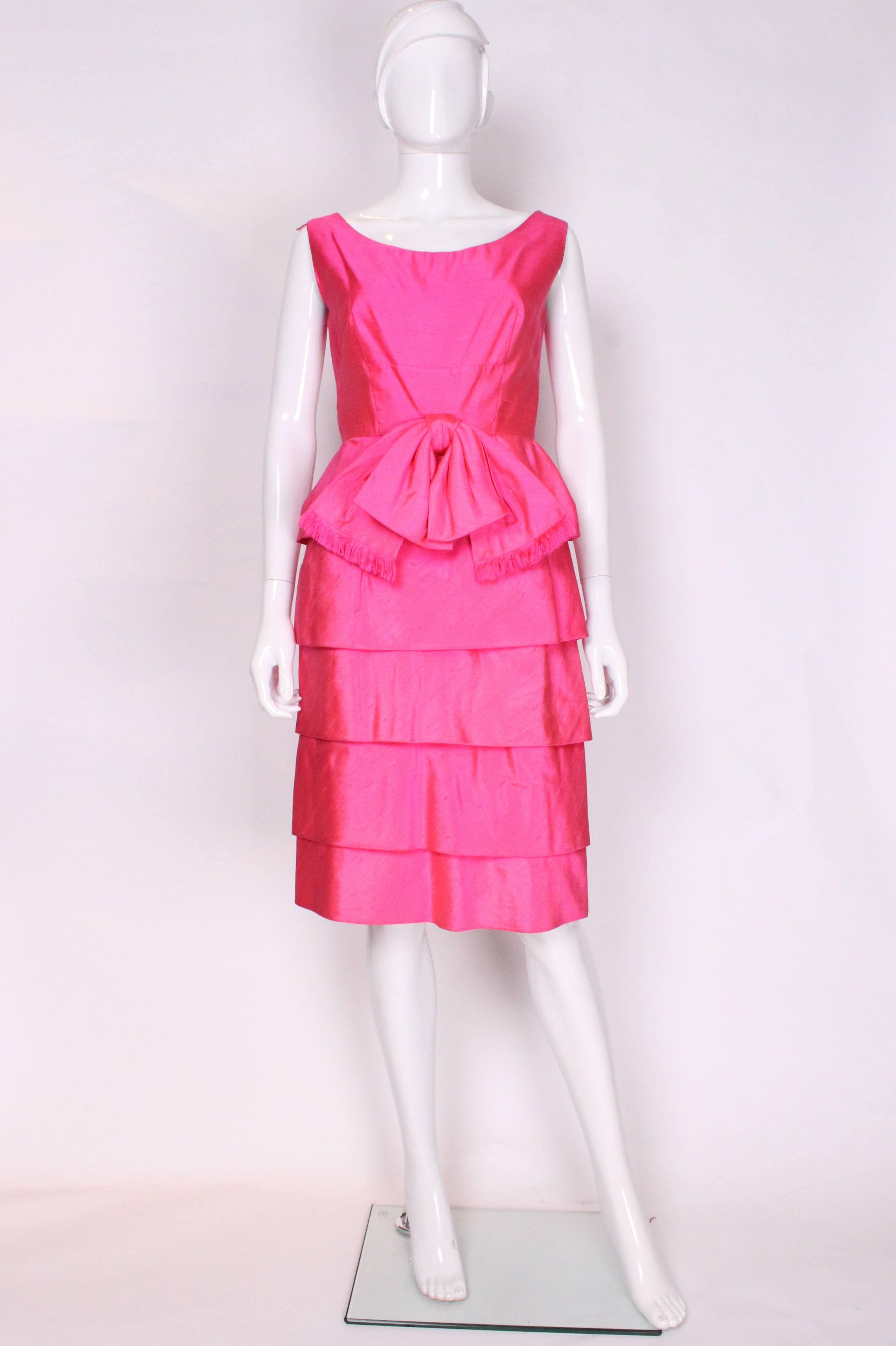 A chic cocktail dress in a wonderful pink raw silk. This dress was made for Harrods. It has a deep boat neckline, a pretty tired skirt with  5 tiers, and large silk bow at the front. The dress is fully lined with an internal waist band and central