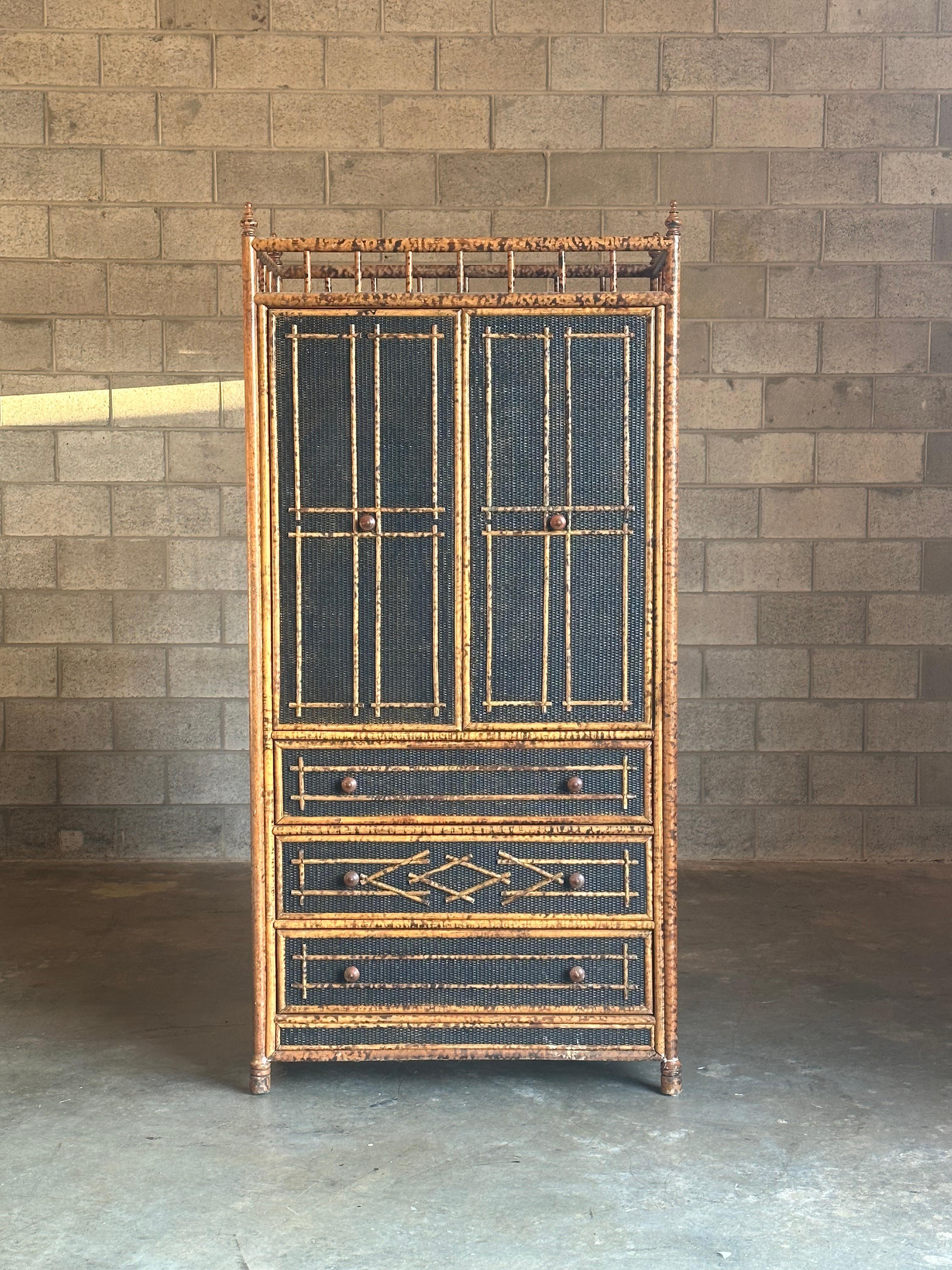 A gorgeous tall cabinet in the British colonial style, featuring faux burnt bamboo and black painted cane. Piece has a number of delightful details, including geometric patterns on the front and sides in the well adorned top. Use as a tv cabinet, a