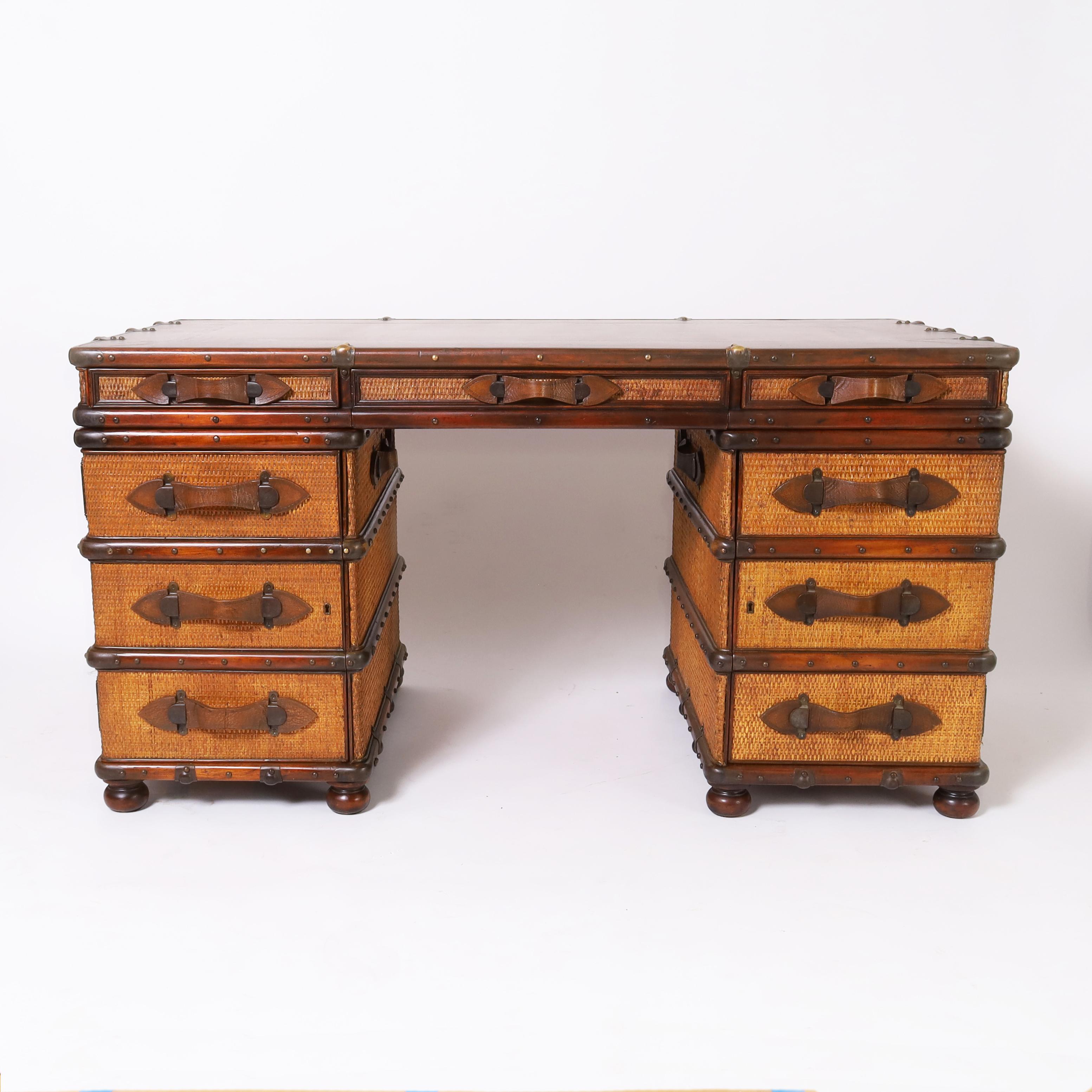 Impressive British Colonial style desk crafted in mahogany in a three piece construction with a tooled leather top featuring burnished brass hardware, leather strap pulls on the three drawers and two doors, woven grasscloth panels all around, two