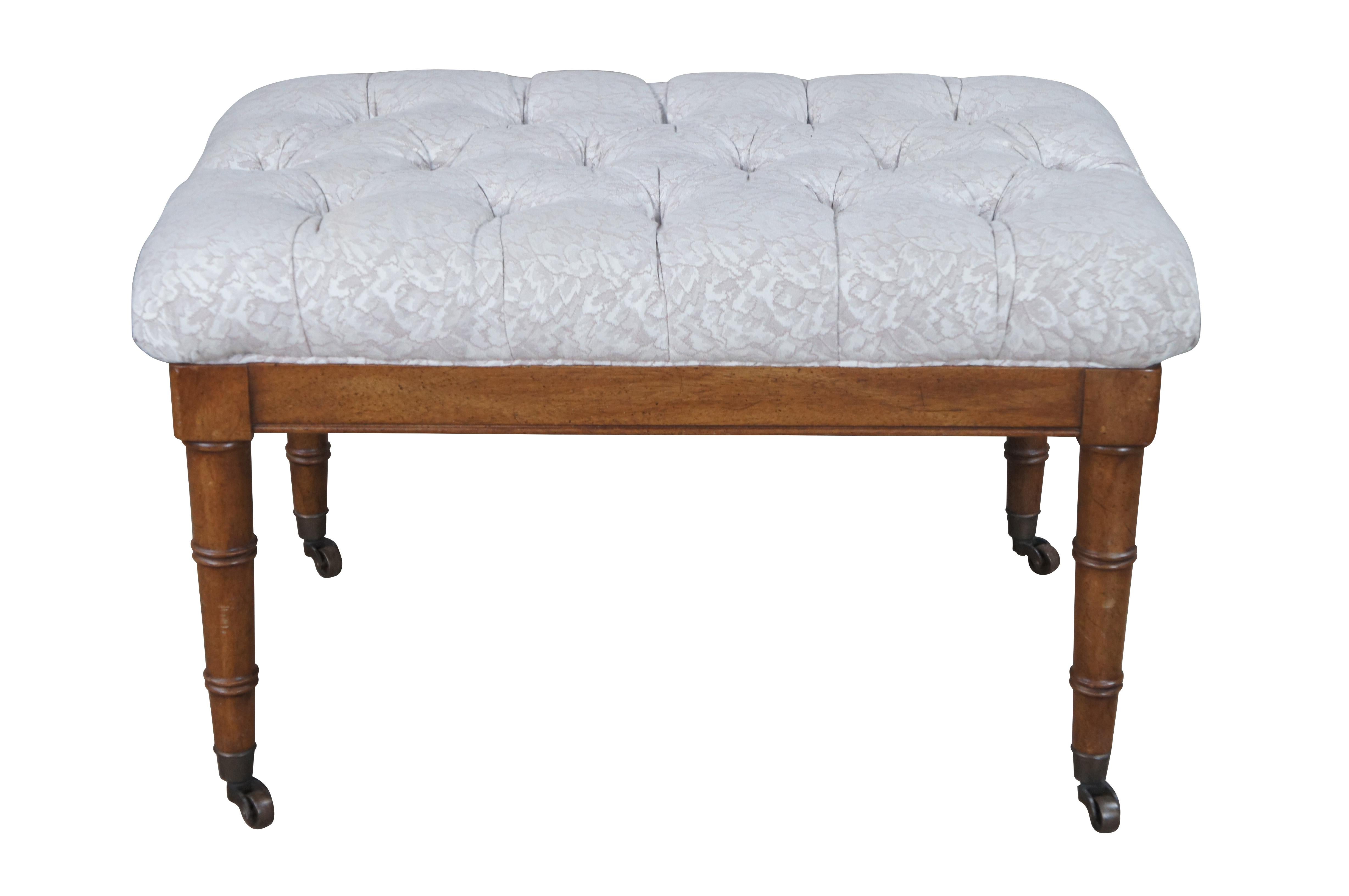 British Colonial style ottoman or footstool, circa 1980s.  Features a rectangular distressed mahogany frame with floral upholstered and tufted pillow top.  The bench is supported by tapered, ribbed legs with brass casters.  

Dimensions:
27