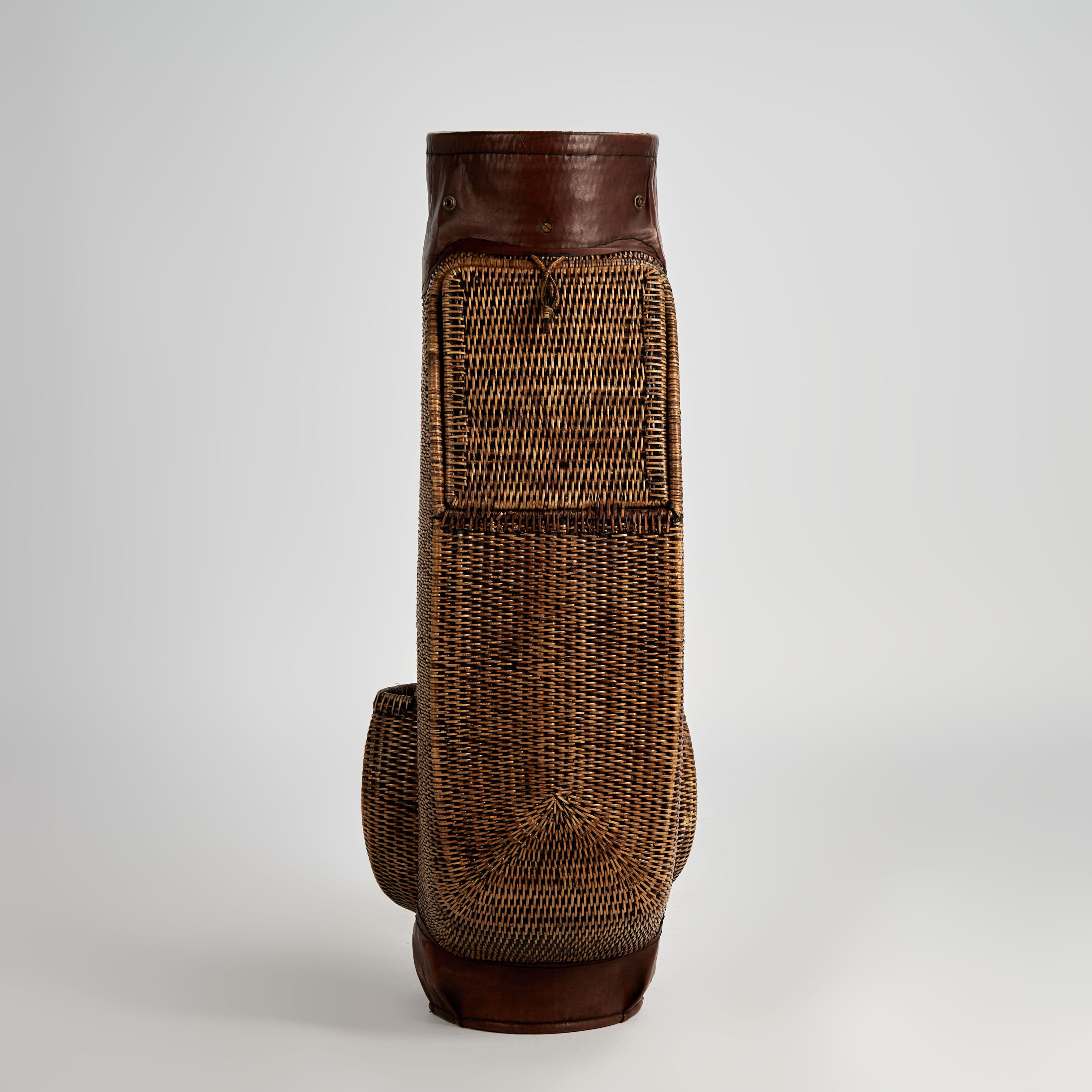 Dapper vintage British colonial style golf bag crafted in wicker with compartments for balls and tees, having a leather strap and collar highlighted with metal snaps and hooks. 