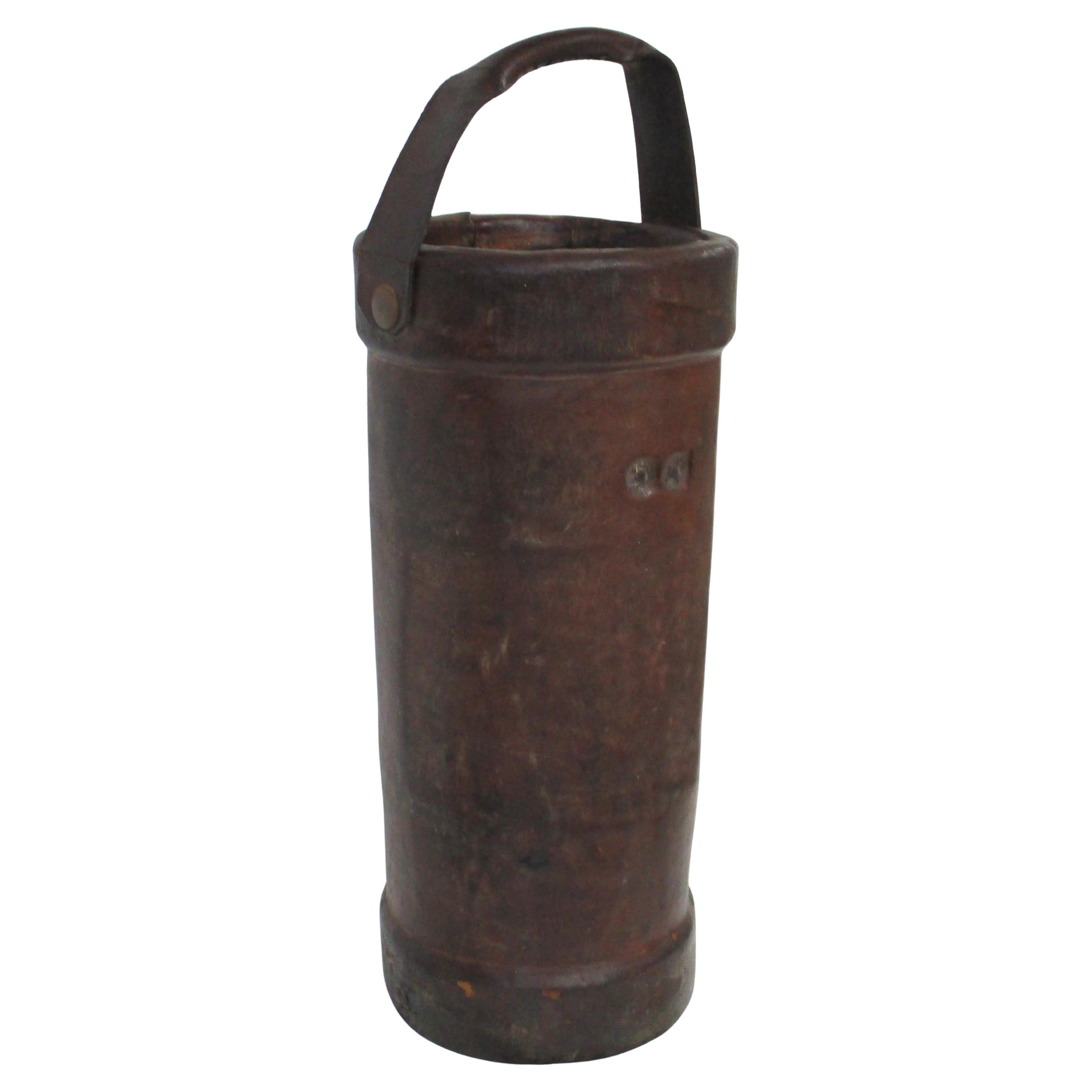 A handcrafted thick saddle leather vintage British fire , powder bucket with handle and canvas interior . A matching strap handle with grommets attach it to the container which can be used as a umbrella stand , walking cane collection holder or for