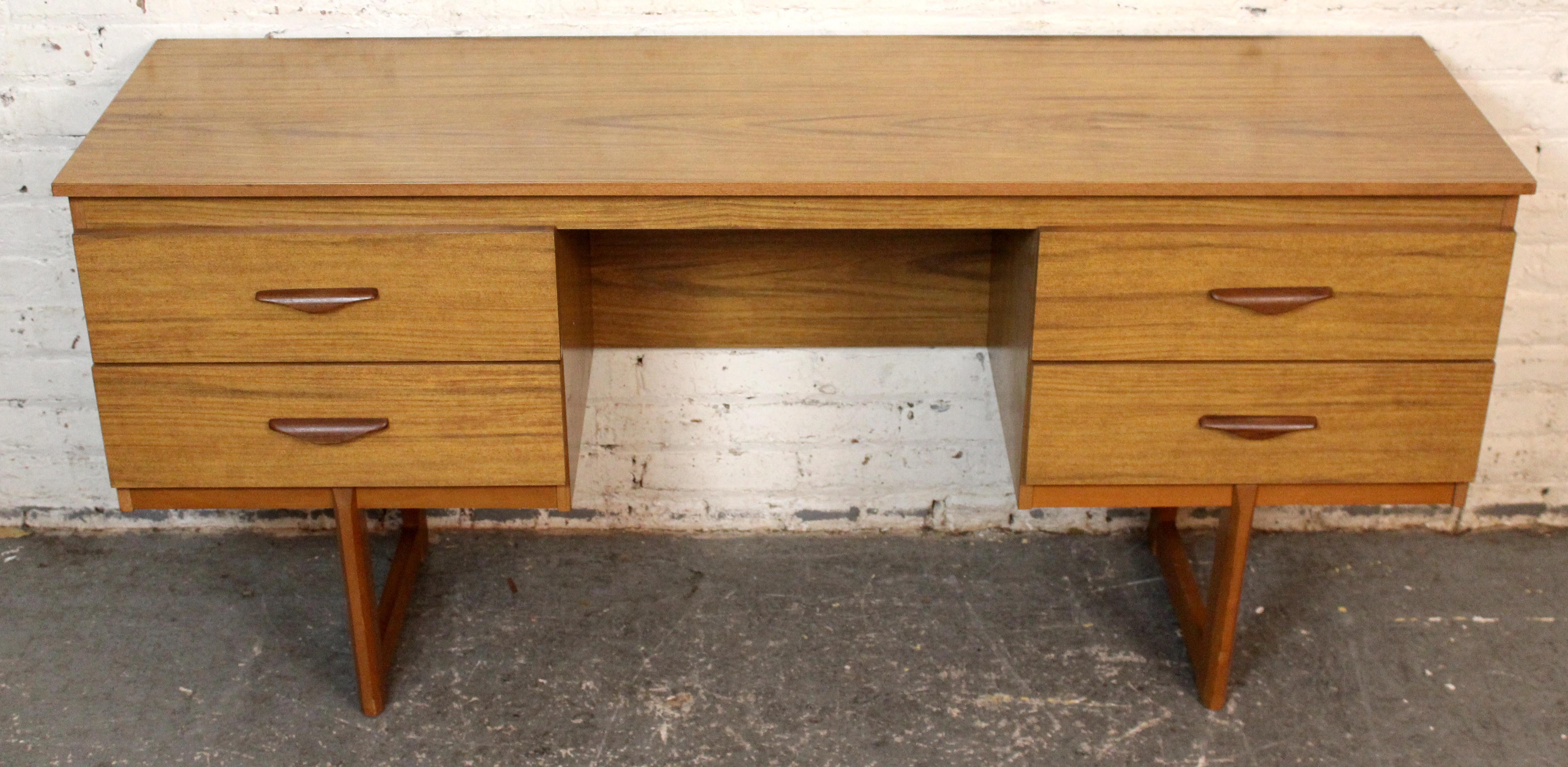 Dieser Vintage-Schreibtisch ist ein klassisches Beispiel für britisches Design aus der Mitte des Jahrhunderts. Er ist mit einem Furnier aus Holzimitat versehen und bietet sowohl Stil als auch Haltbarkeit. Mit seinen vier großzügigen Schubladen mit