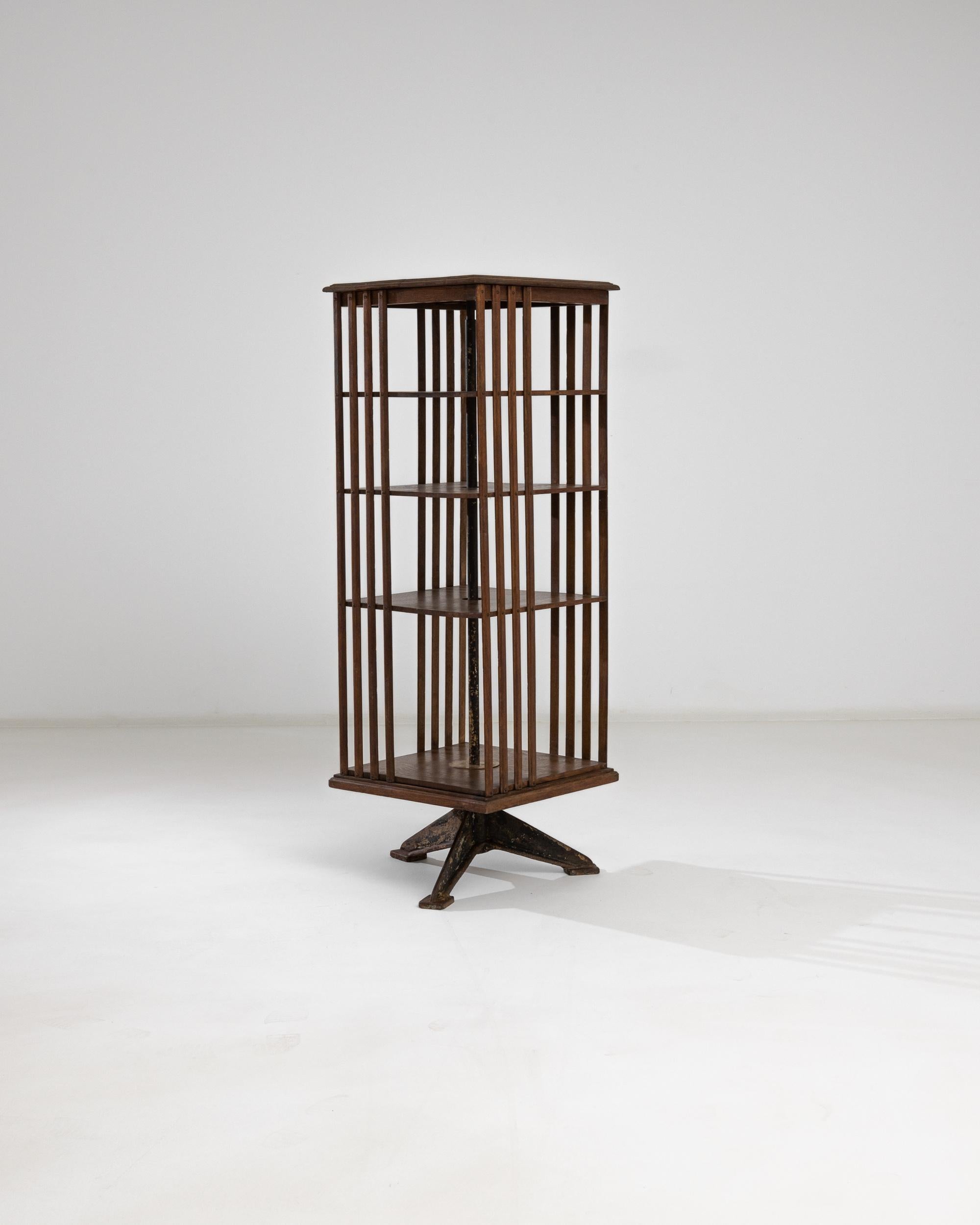 A wooden shelving unit from the United Kingdom, produced circa 1900. Standing on a patinated metal tripod stand, tall wooden rods elevate from an elegantly beveled square base. The nobly preserved wood exhibits a rich chocolate tone with tawny hues,