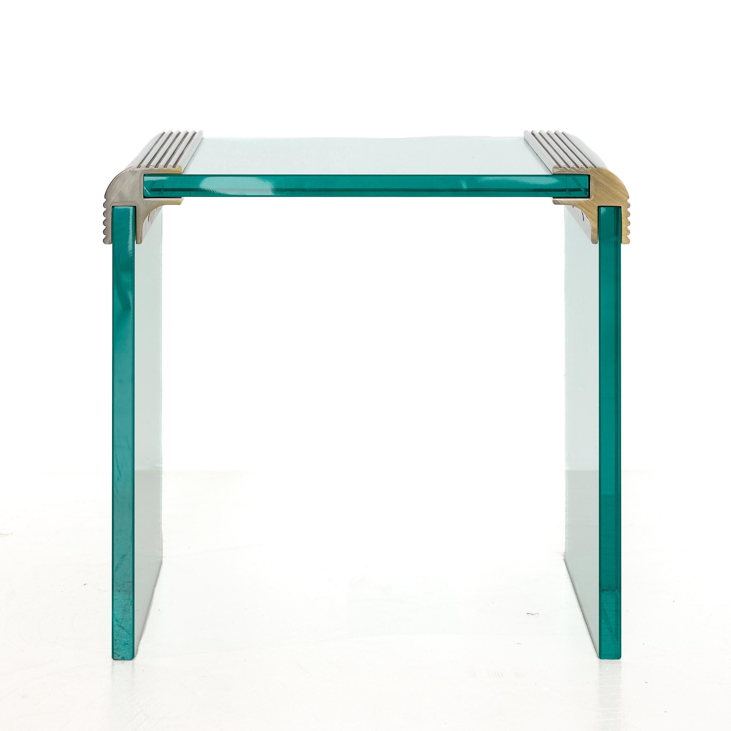 Schlanker, postmoderner Wasserfall-Akzent- oder Beistelltisch im Design der 1980er Jahre mit Platte und Seitenteilen aus schwerem gehärtetem Glas und geschwungenen Eckwinkeln aus vergoldeter Bronze.  
Das flaschengrüne Glas lässt das Licht