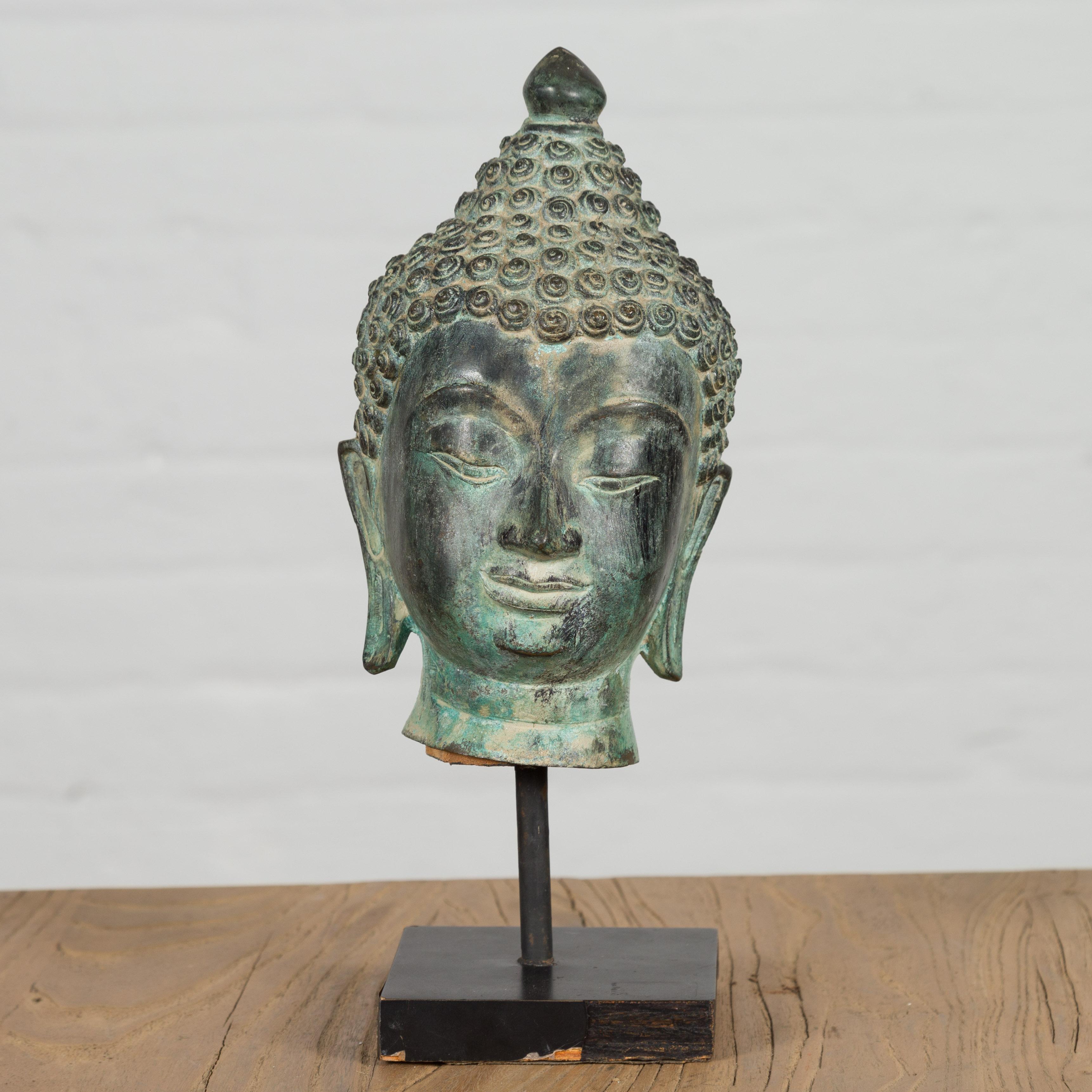 A vintage bronze Buddha head sculpture on custom base, with verdigris patina, made with the lost wax casting process. Experience serenity and grace with this vintage bronze Buddha head sculpture that exudes an aura of spiritual transcendence. The