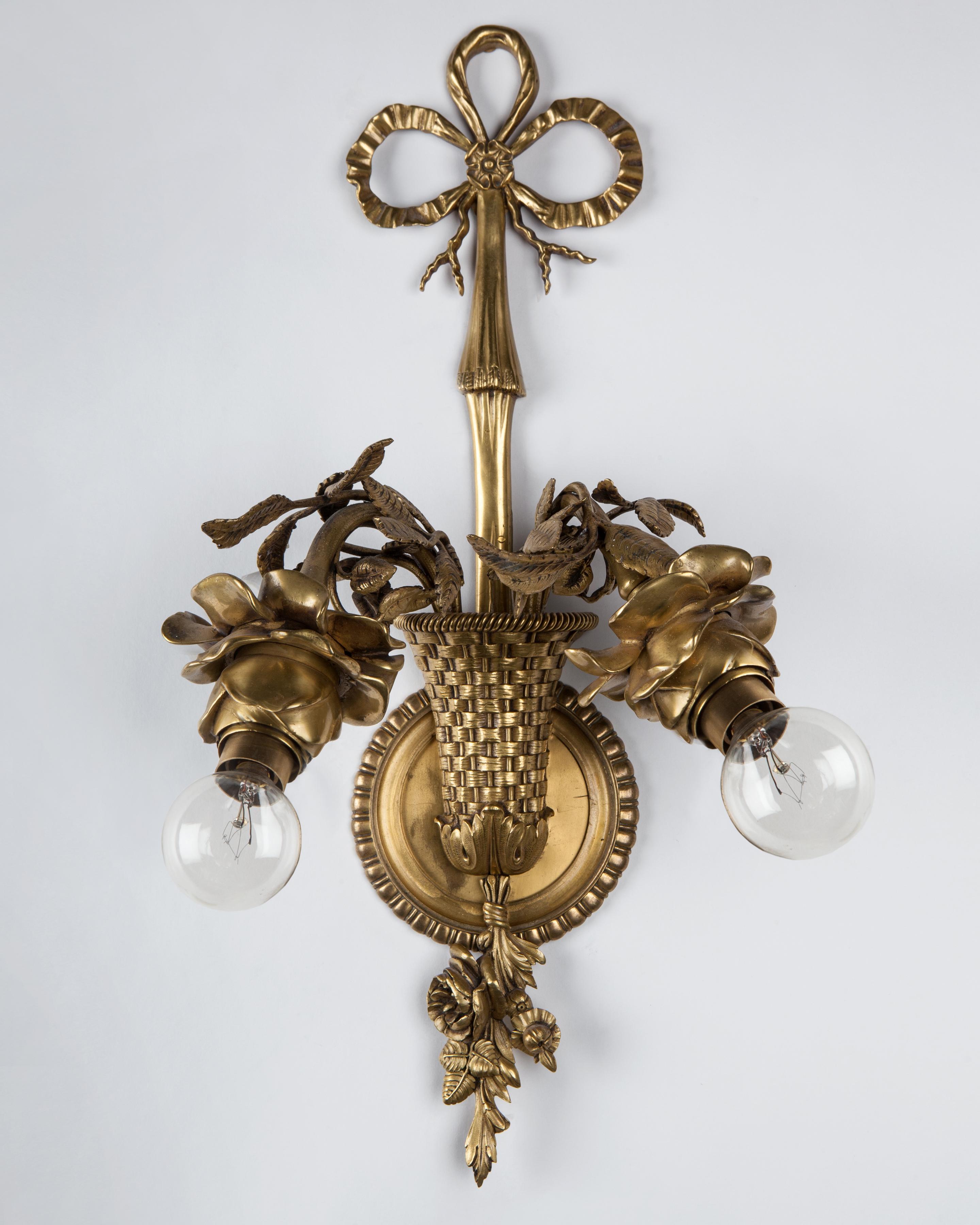 AIS3040
A pair of antique sconces with intricately detailed blooming rose socket cups springing from woven baskets. Having cast bronze gadrooned backplates with bow finials and foliate tassels. In their original aged gilded finish. Attributed to the