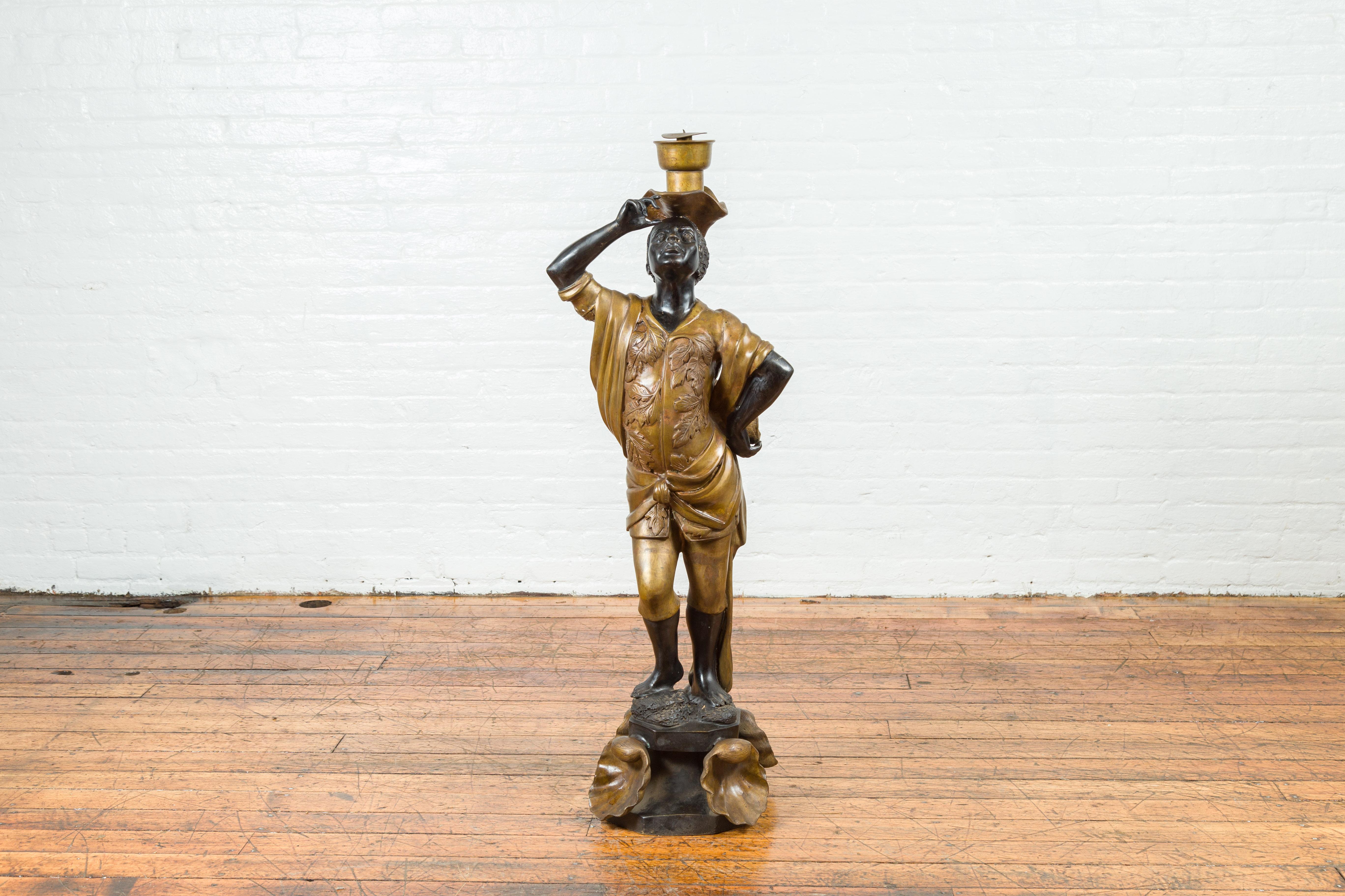 A vintage bronze candleholder statue with black and gold patina, on shell base. Created during the 20th century with the traditional technique of the lost-wax (à la cire perdue) that allows a great precision and finesse in the details, this