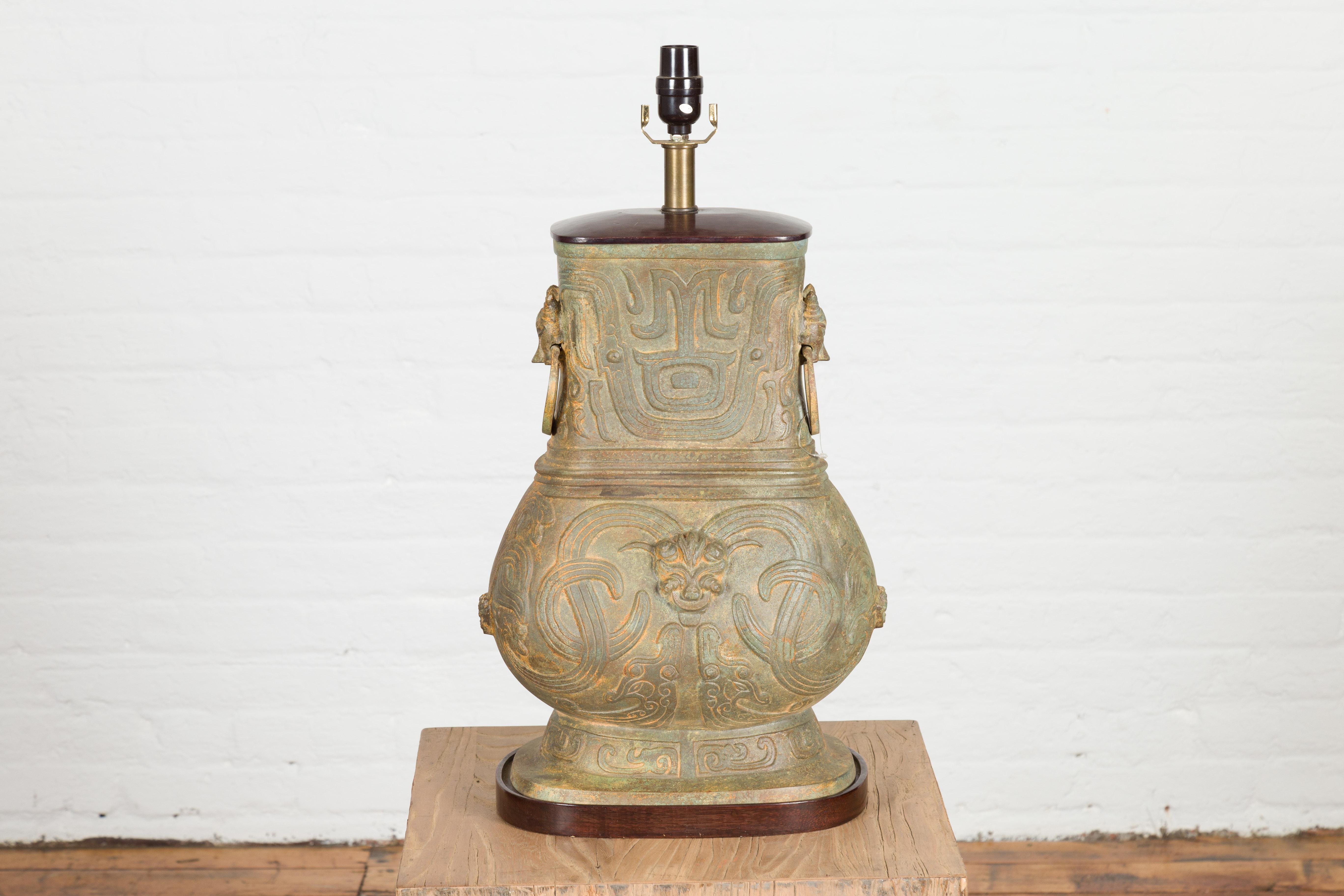 A vintage cast bronze Chinese Hu vessel style table lamp from the Mid-20th Century, with interlinking waves, dragon heads and mythical animals. Wired for the USA, this cast bronze table lamp showcases a sinuous silhouette with a narrow top and wide