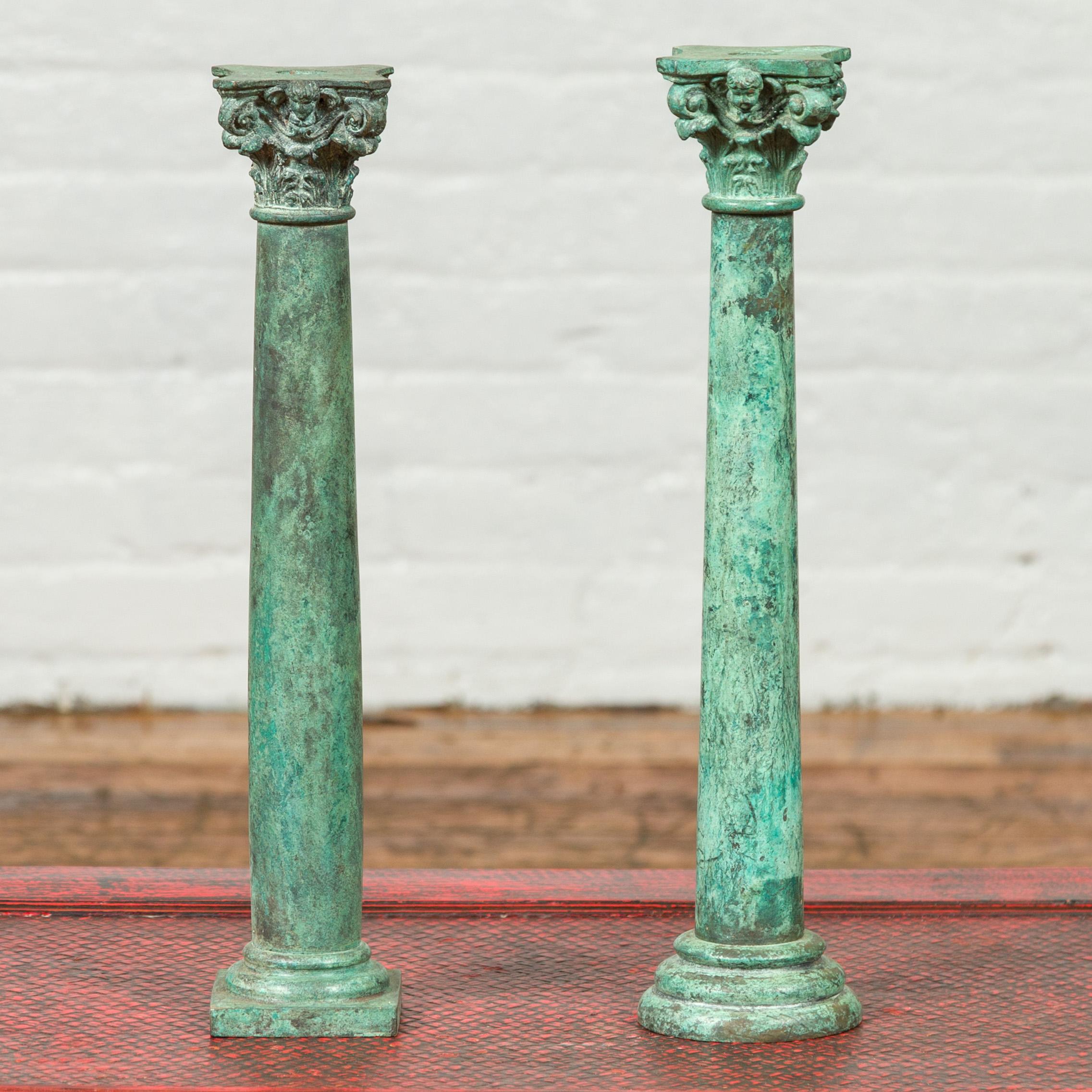Two vintage bronze Corinthian column candlesticks with verdigris patina and cherub motifs, priced and sold individually. Crafted during the midcentury period, each of these two candlesticks features a column with entasis and verdigris patina. Each