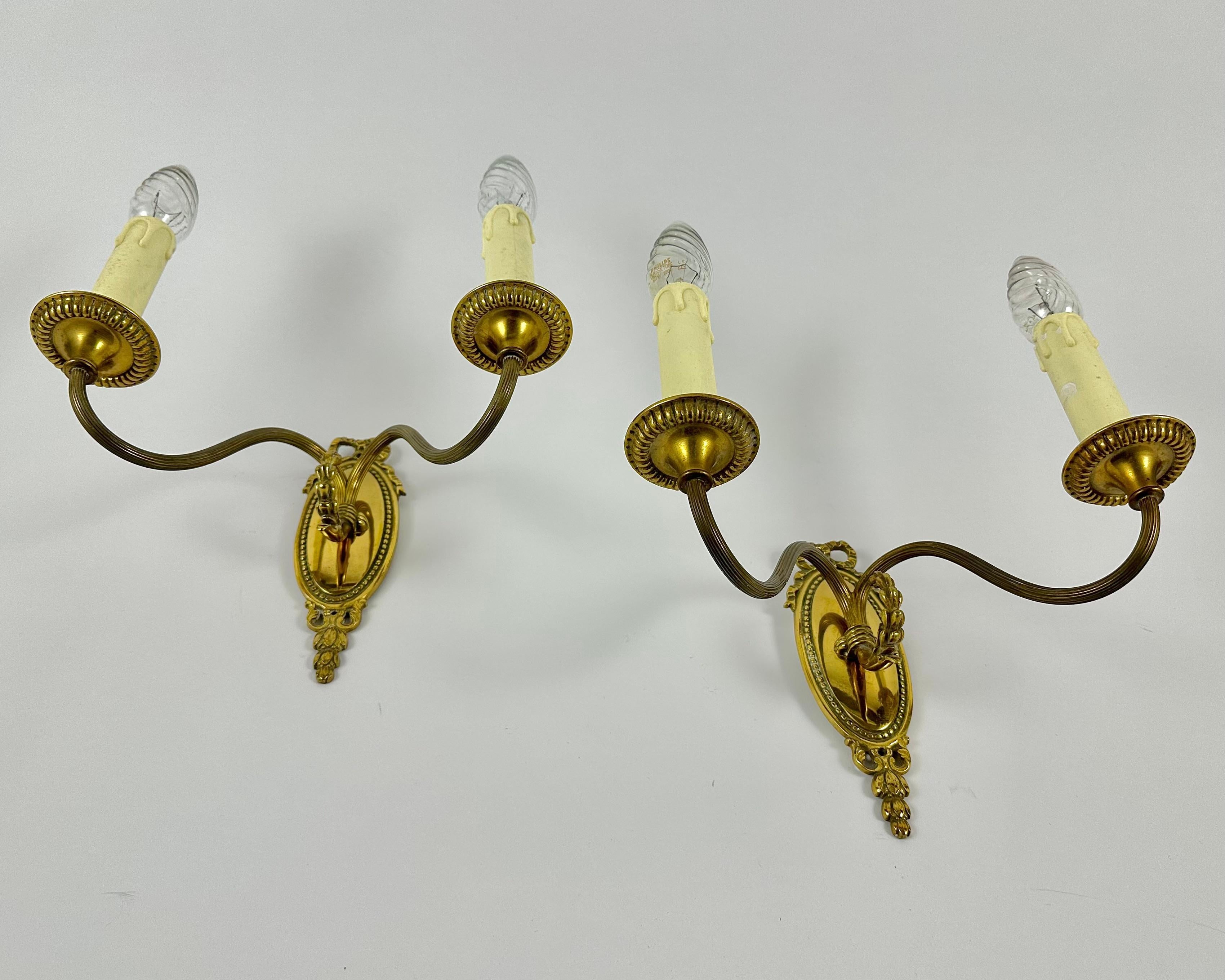 Pair of Belgian Neoclassical or Louis XVI style bronze twin arm sconces from 1970s.

This pair of vintage bronze sconces has a beautiful oval bronze base that has delicate acanthus leaf pattern and a bow.  

Very noble and sensual! Such wall lamps