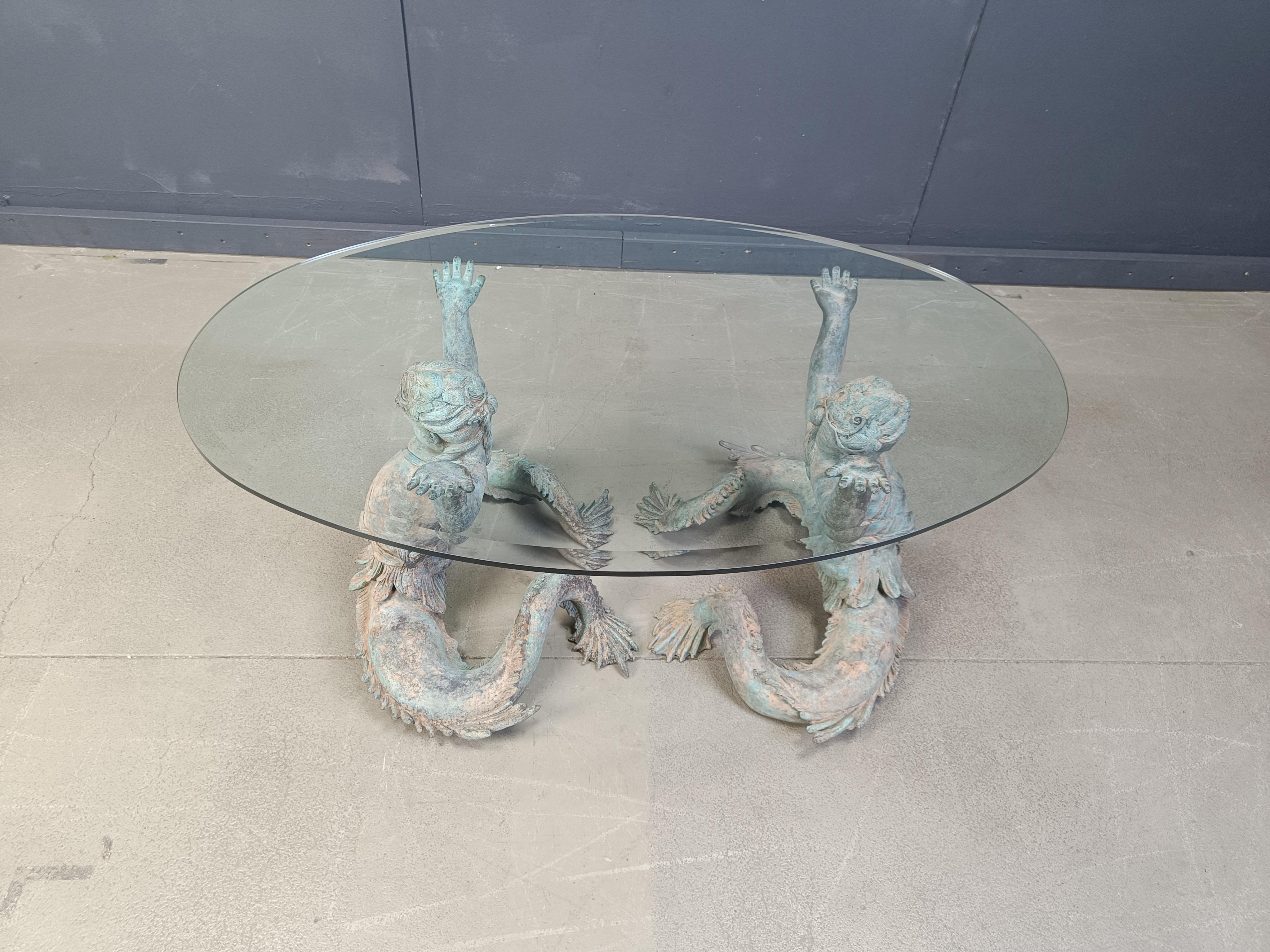 Fantastic Italian nautical cocktail table or coffee table featuring a pair of patinated bronze Putti Di Mare mermaids supporting a thick glass beveled glass.

Nicely detailed sculptures.

1960s - Italy

Dimensions:
Height: 52cm
Width: 120cm
Depth: