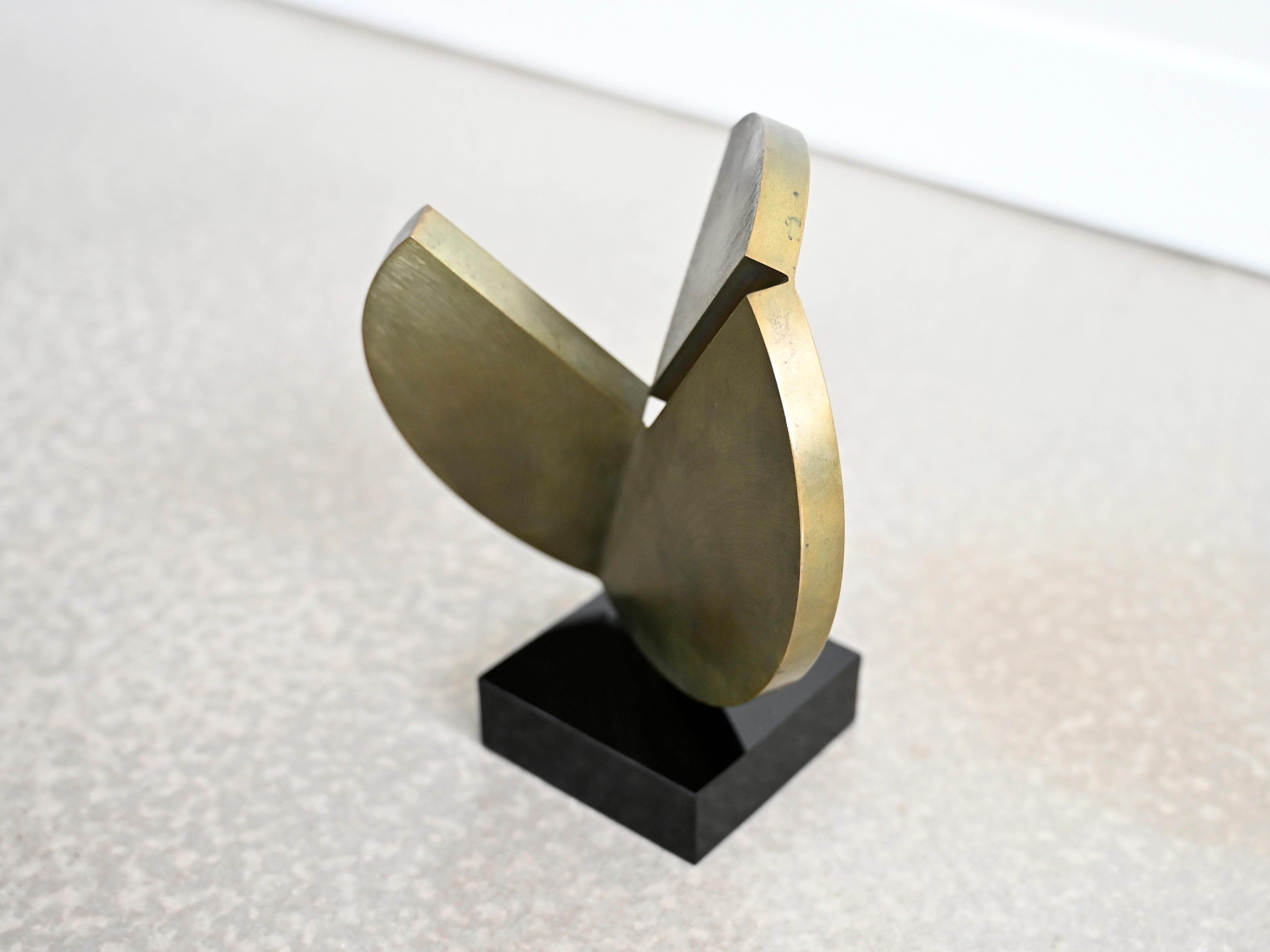 Escultura de sobremesa vintage realizada en bronce macizo fijada a una base de lucita negra. El cuerpo de la escultura presenta una gruesa forma circular de latón cortada y doblada en direcciones opuestas. Firma de artista grabada a lo largo del