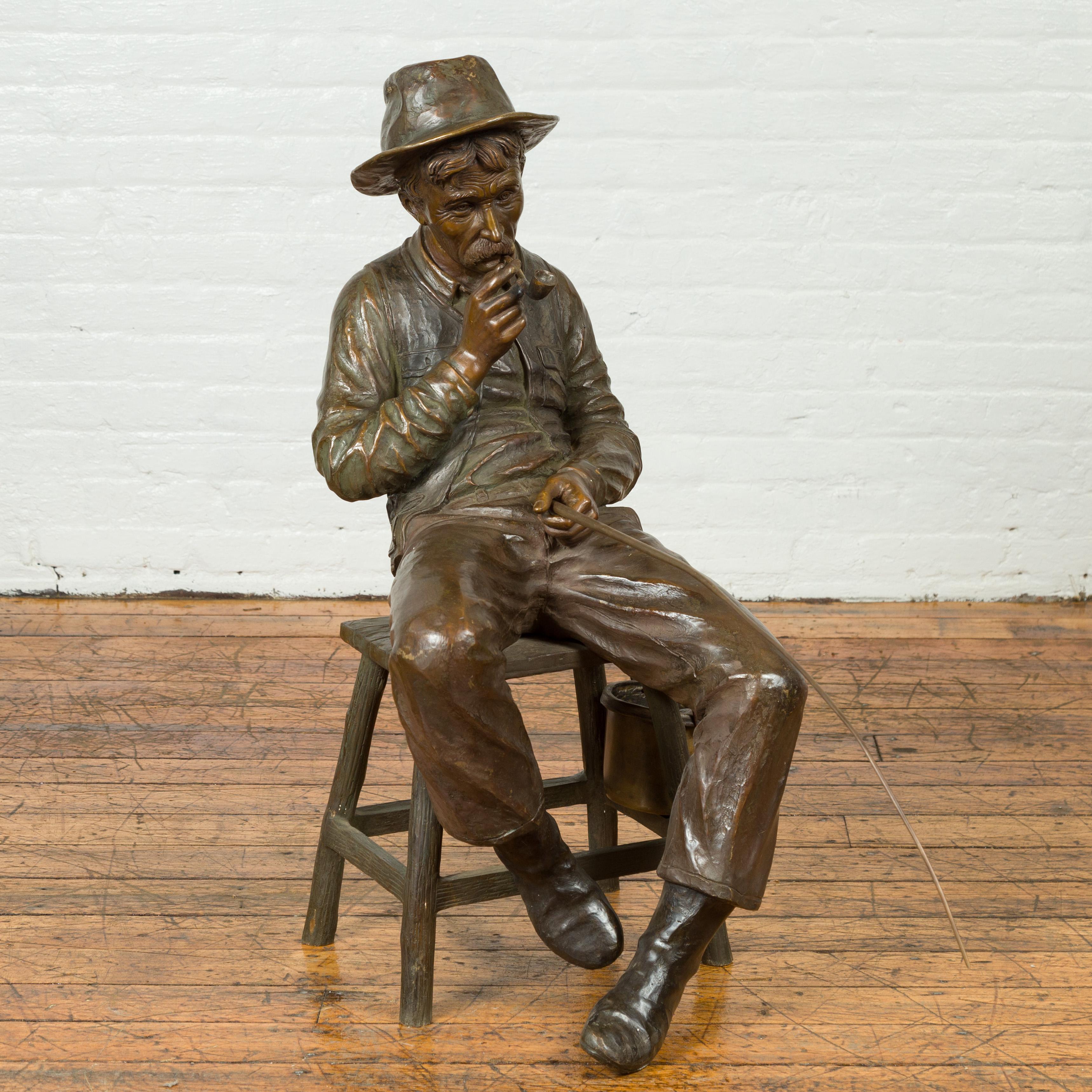 A vintage bronze sculpture of an old timer smoking his pipe and fishing. Perfect to be placed in a garden, this 20th century bronze sculpture will bring a heartwarming presence to any setting. A man, smoking his pipe and sitting on a rustic stool,