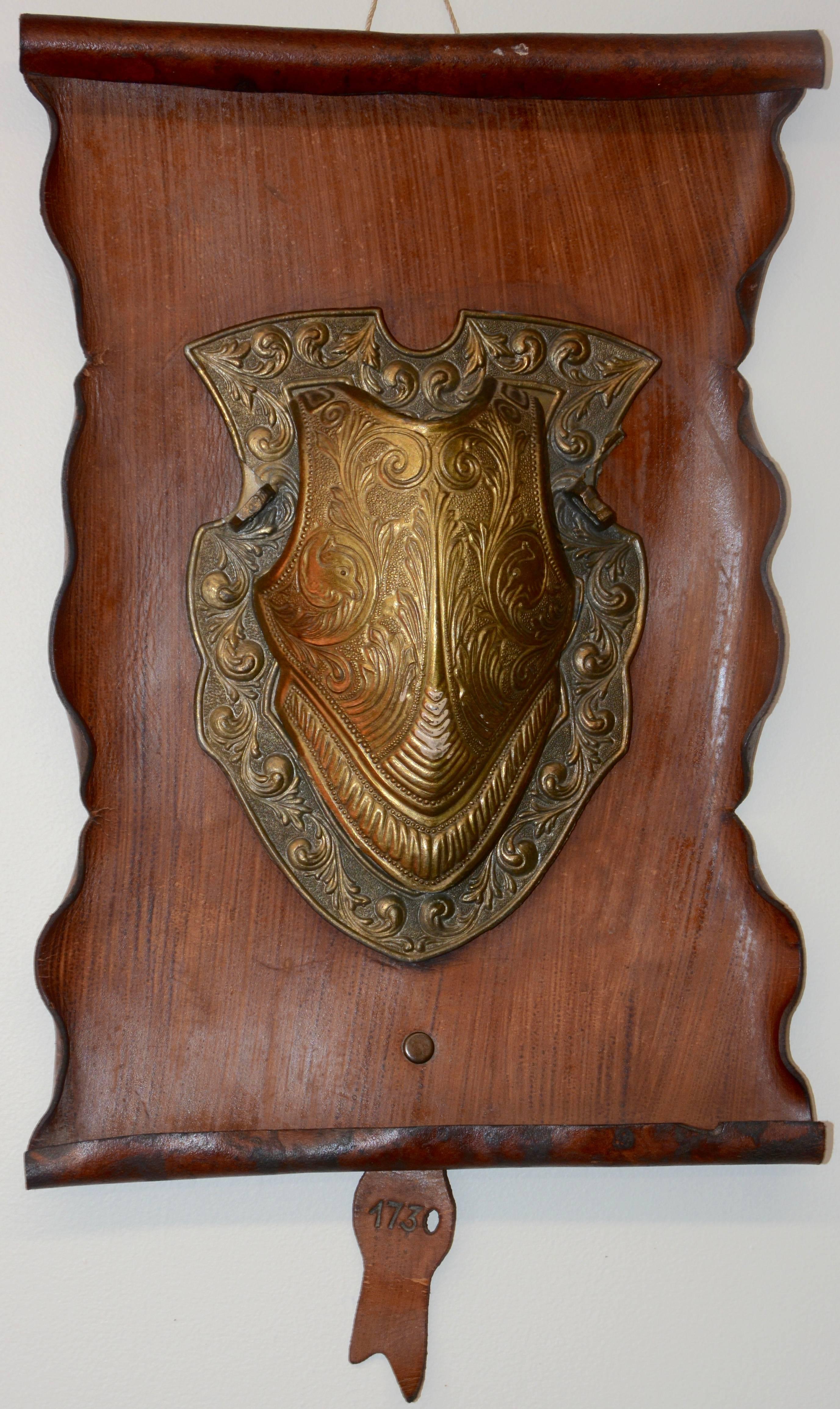 We are offering a vintage reproduction of a bronze shield mounted on a rustic leather scroll. The leather has rolled edges top and bottom and the sides are cut and folded. There is a leather tab on the bottom date 1730 which is most likely the date