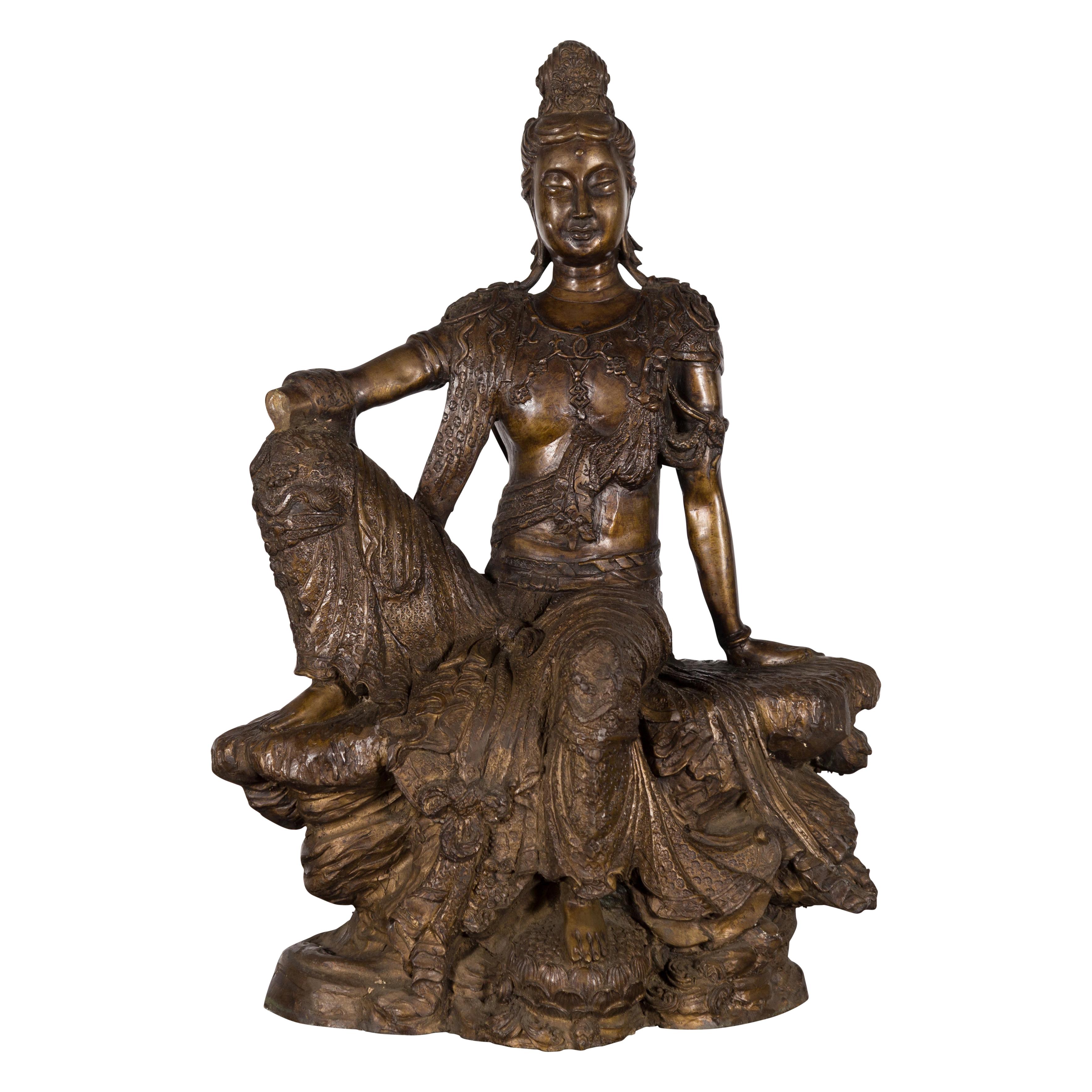 A vintage bronze statuette from the mid-20th century depicting Quan Yin. Created during the midcentury period, this bronze statuette features the Quan Yin, the Goddess of Compassion, depicted in a seated position. Wearing ornate clothes and