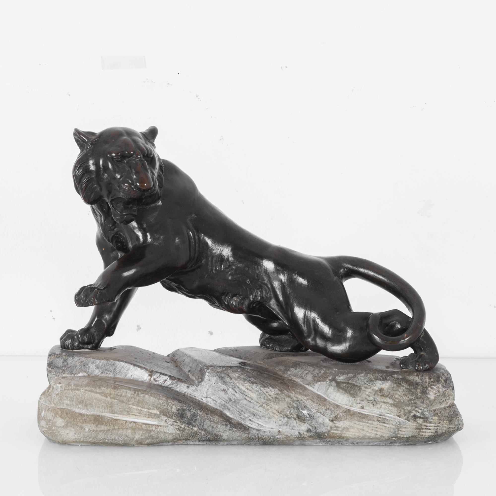 This bronze tiger sculpture on a stone was made in France, and will make an impressive statement in any interior space. The tiger, with open jaws, has its left front paw lifted, and its head looks over the left shoulder. The stone has a smooth