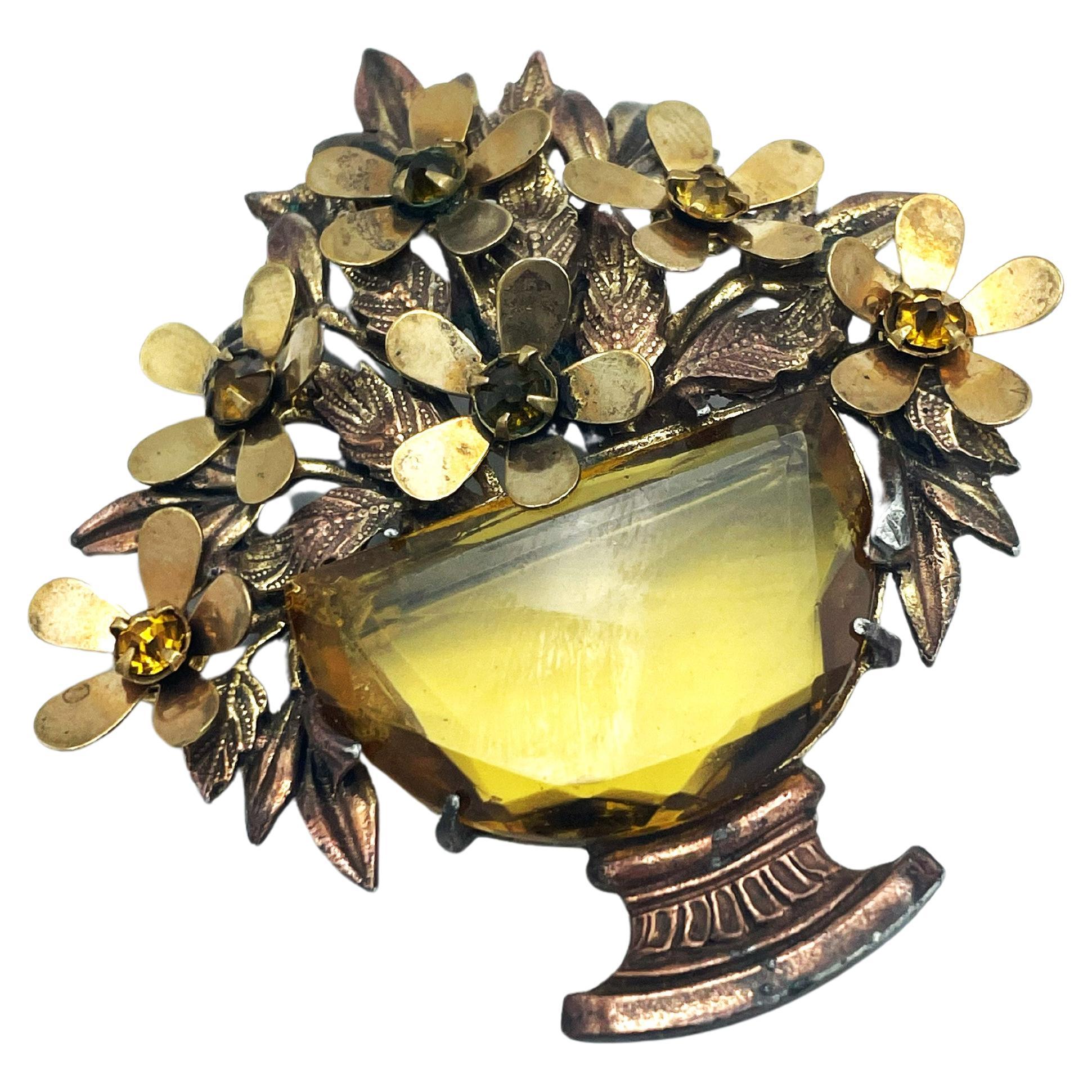 Brooch in the shape of a flower basket with a large topas  cut rhinestone as the flower vase inside are golden flowers with small gold rhinestones.
The brooch was designed in the USA in 1940, is unsigned and shown in 