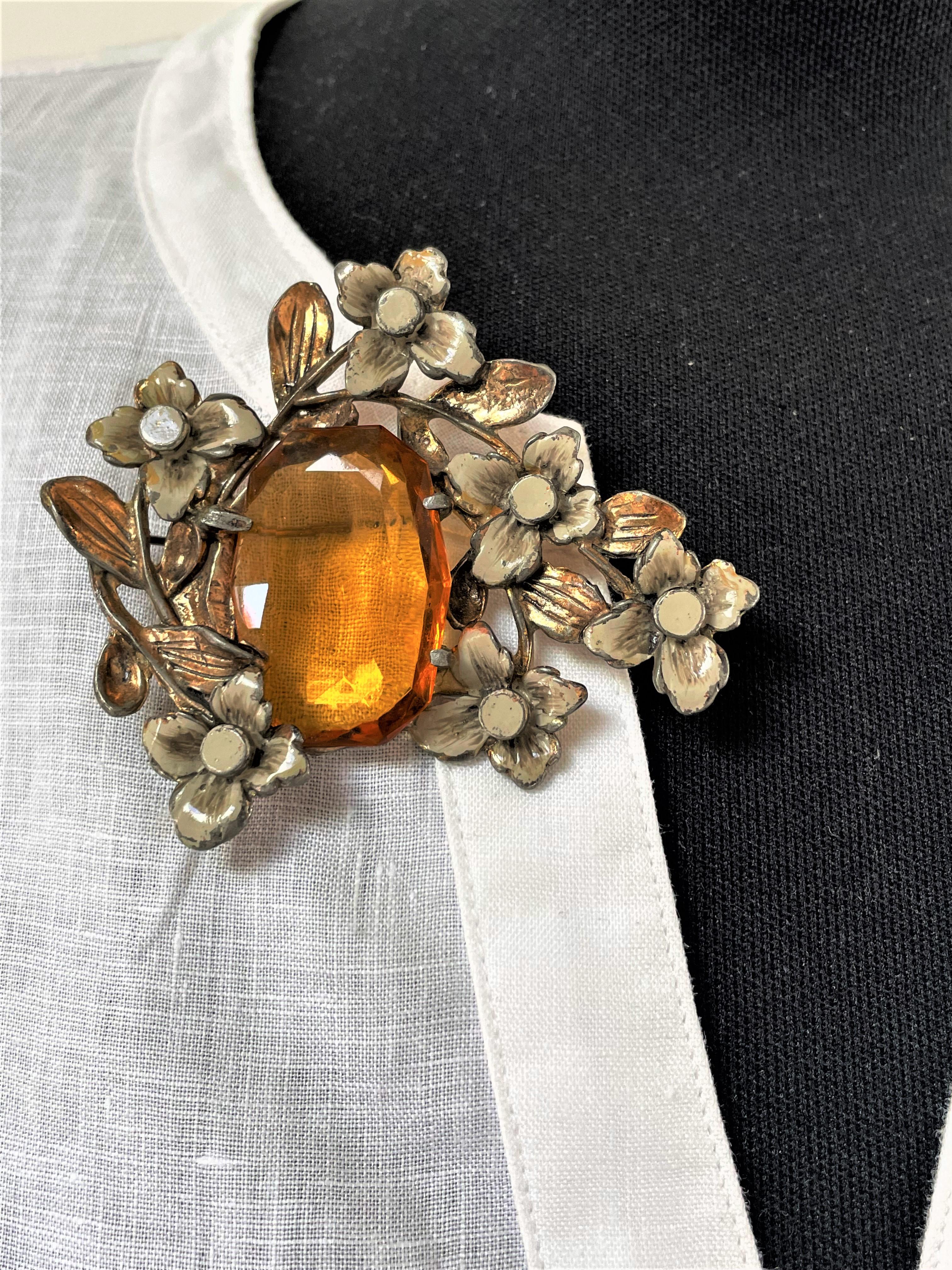 An enchanting vintage brooch from the early 1930/40s in the USA. In the middle is a large rhinestone that is cut on both sides. Bordered with 6 enameled flowers and leaves. A beautiful unit rhinestone stone and gold-colored border.
Measurement: