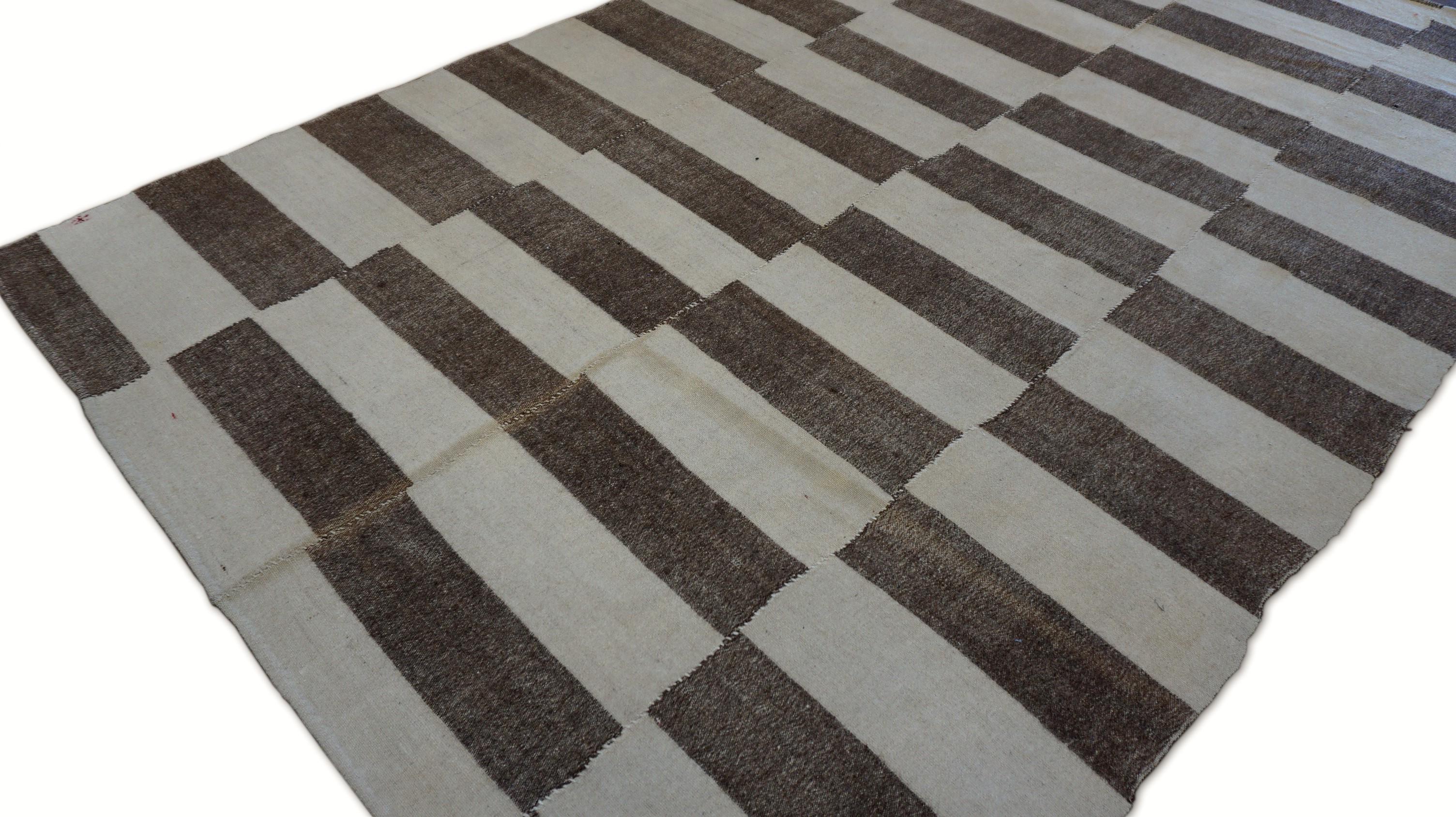 This striking handwoven wool flatweave showcases a bold geometric rhythm through its alternating horizontal stripes of rich brown and warm ivory. Arranged in stacked offset blocks across vertical columns, the design offers a contemporary graphic