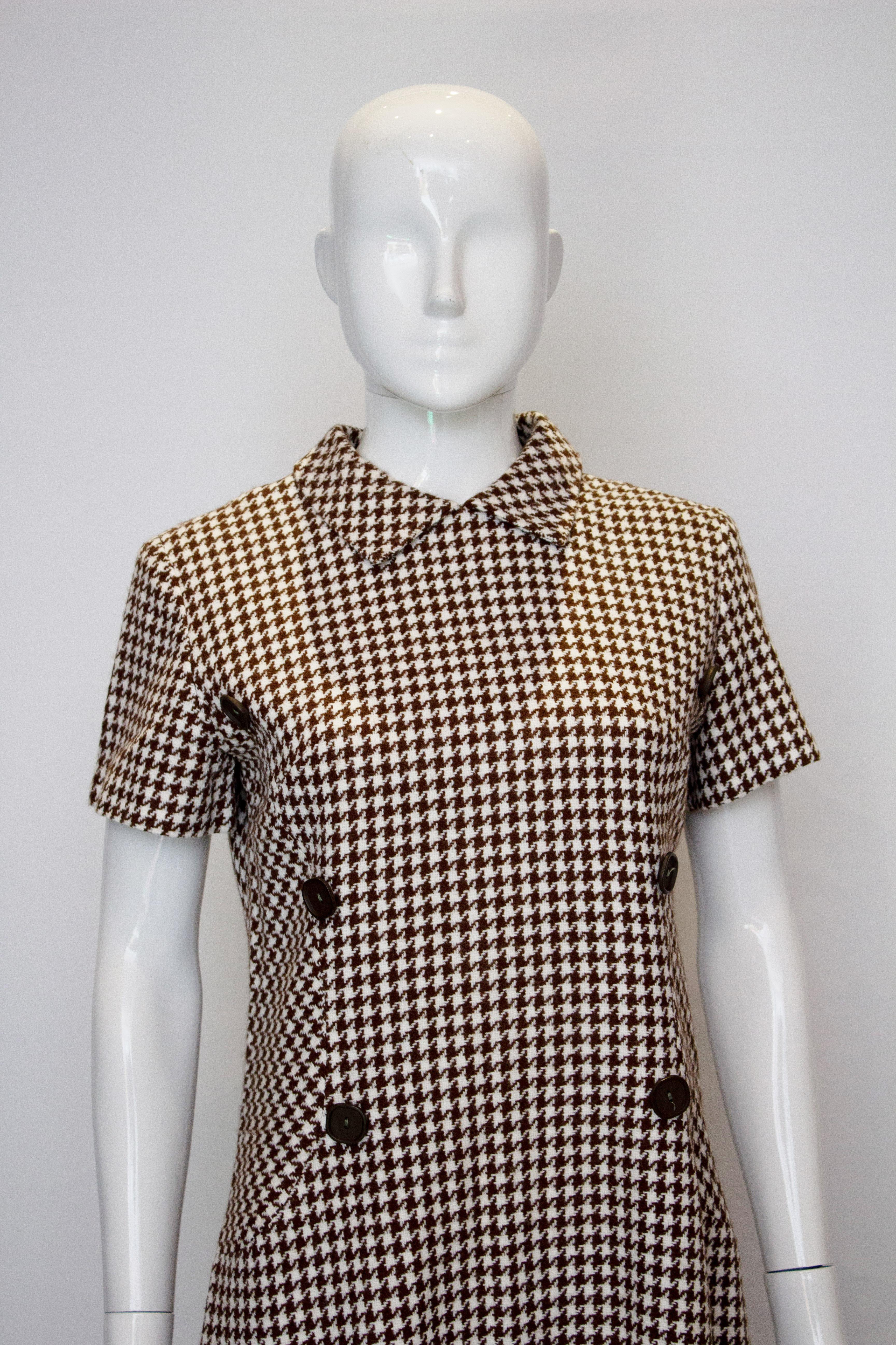 A chic day dress by Nancy Green in brown and white houndstooth. The dress has a central back zip opening and six decorative buttons on the front.