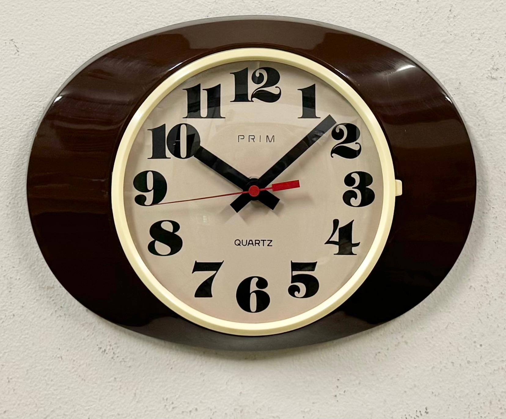 Cette horloge murale vintage en bakélite a été fabriquée par Prim dans l'ancienne Tchécoslovaquie dans les années 1970-1980. Whiting présente un corps en bakélite brune, un cadran en bakélite blanche et un couvercle en verre transparent convexe. Le