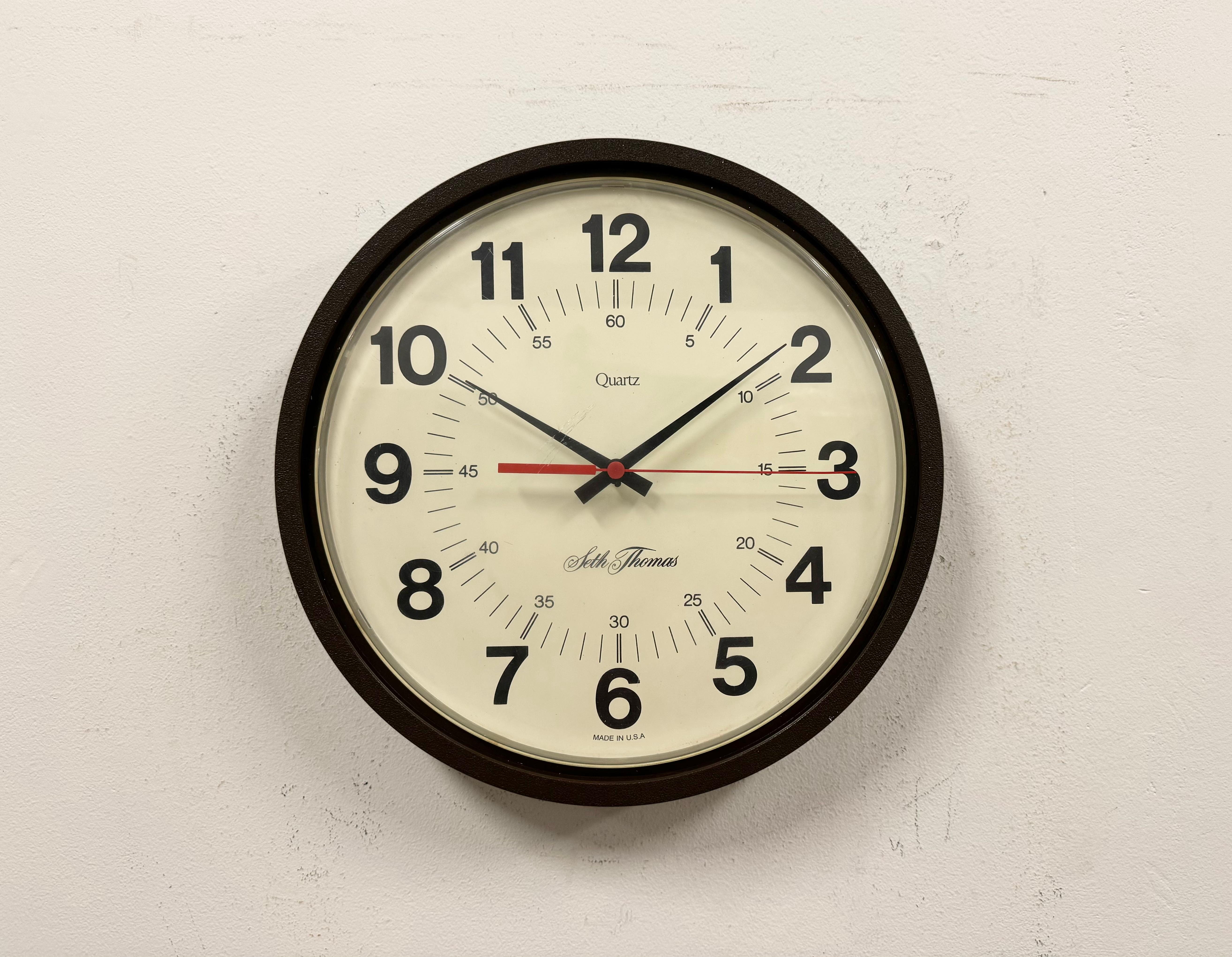 Horloge murale vintage en bakélite fabriquée par Seth Thomas Clock Company aux Etats-Unis dans les années 1980, avec un boîtier en bakélite marron foncé et un couvercle en verre en plastique transparent. Le mécanisme d'horlogerie fonctionne avec une