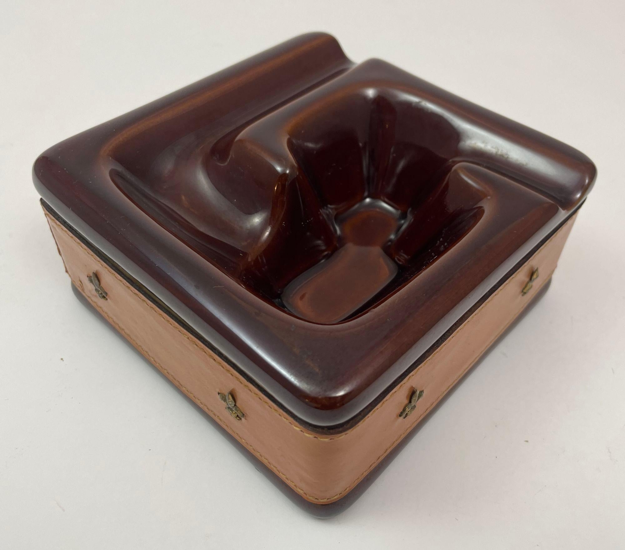 Vintage brown ceramic cigar or pipe ashtray wrapped in saddle leather with contrast stitching and brass fleur de lys decor.
Perfect saddle leather ashtray catchall vide poche or just use it as a great sculptural decorative piece dish.
Dimensions of