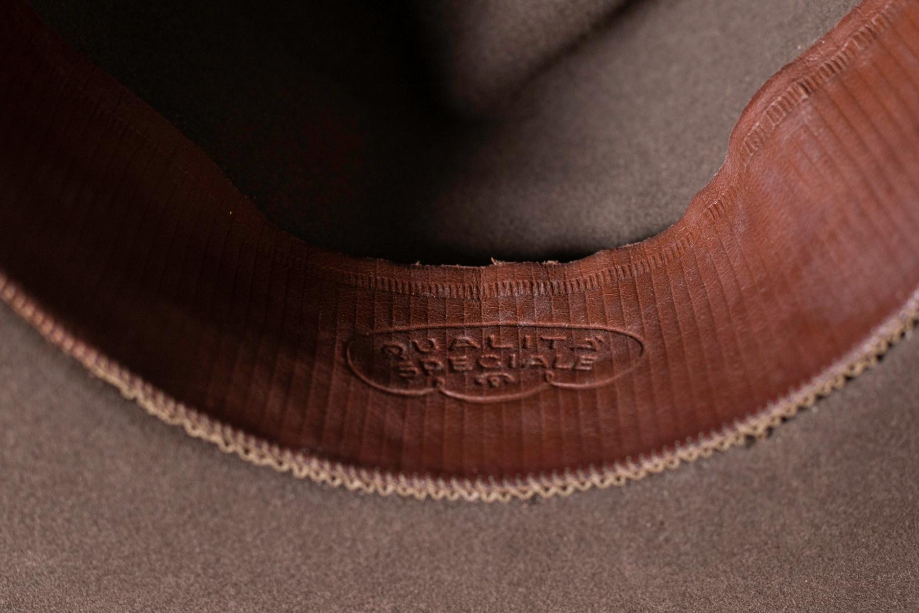Feiner, in Italien hergestellter Hut aus braunem Stoff aus den 1990er Jahren.
Der Hut ist vollständig aus Stoff gefertigt.
Die Kuppel trägt 4 weiche Zacken.
An der äußeren Basis der Kuppel befindet sich ein glänzendes braunes Band.
Im Inneren der