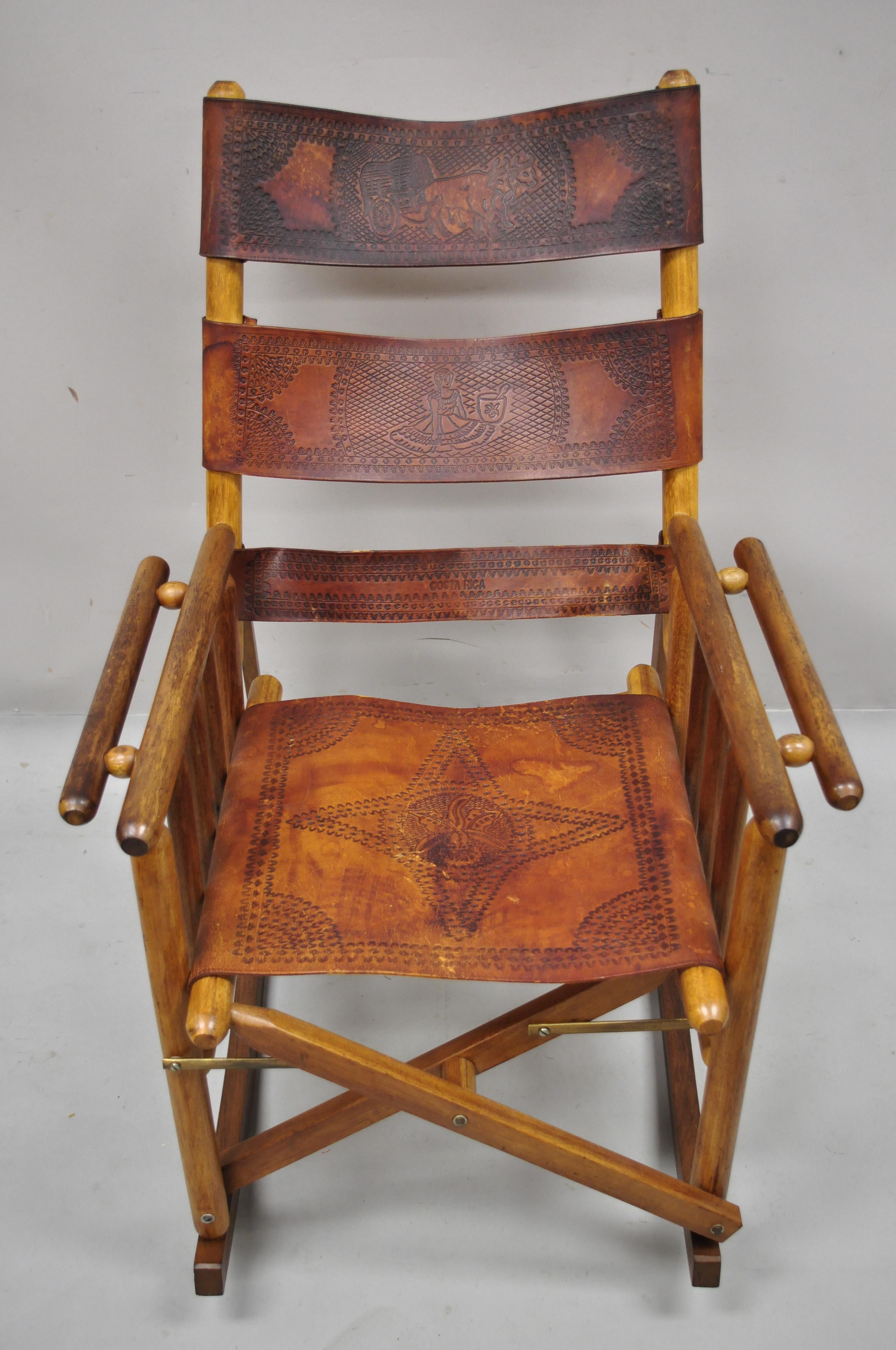Vieille chaise à bascule pliante costaricaine en cuir brun style campagne. L'article présente un cadre en bois d'acajou:: des sangles en cuir brun:: un design pliant:: des gravures sur le cuir:: un très bel article vintage:: un grand style et une