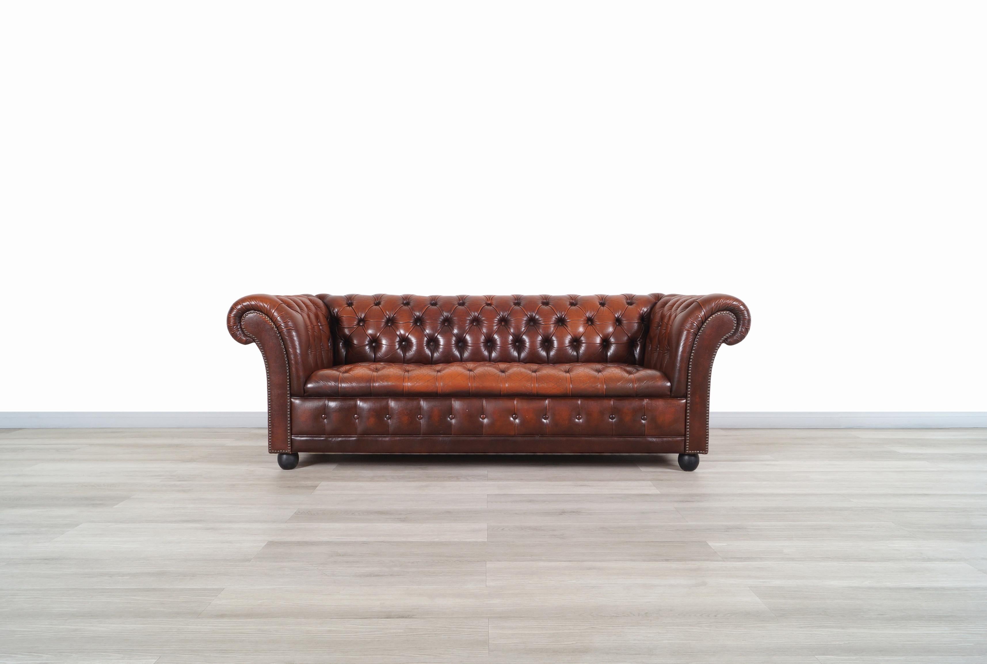 Elegant vintage leather chesterfield sofa manufactured in Great Britain, circa 1950s. This sofa has a design where the elegant arrangement of the deep tufted diamond upholstery through its structure makes it stand out even more. Features brass