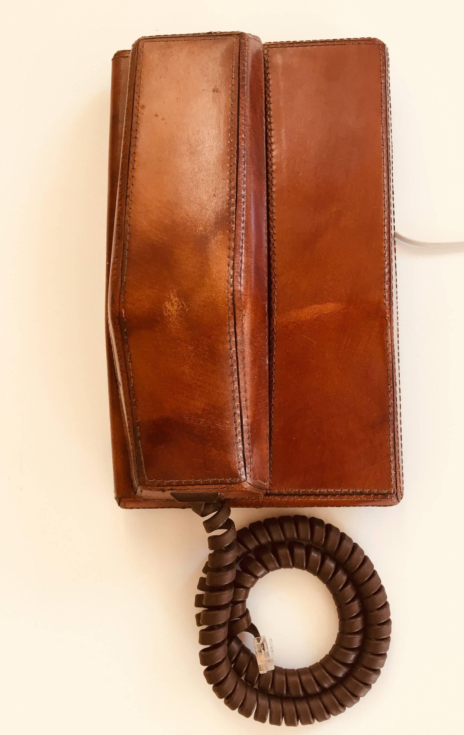 Vintage Northern Telecom Contempra telephone covered in stitched brown leather.
The keypad is located on the underside of the handset.
Could be used on a desk or wall.
Great decorative vintage masculine look object.
The telephone is covered in