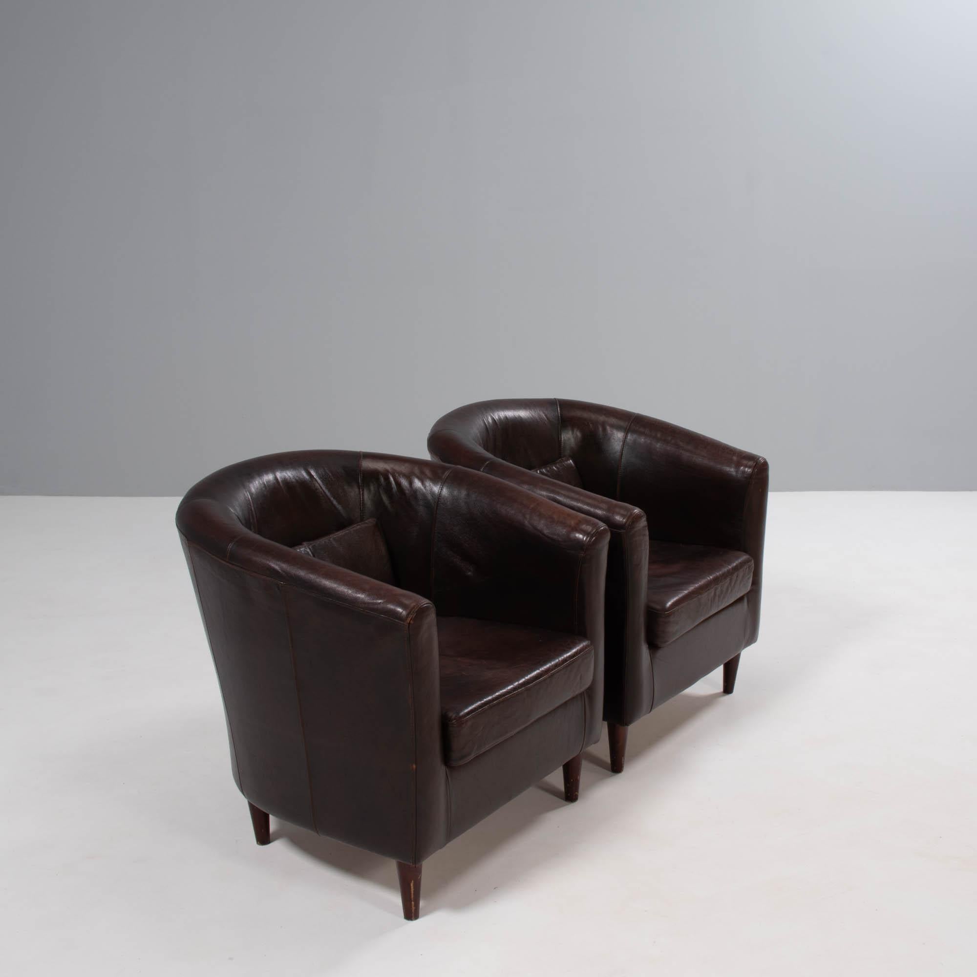 A pair of vintage tub chairs, fully upholstered in dark brown leather with wooden feet.

The chairs have curved backrests and integrated arms, creating the tub silhouette with a seat cushion and additional back cushion for extra comfort.

A