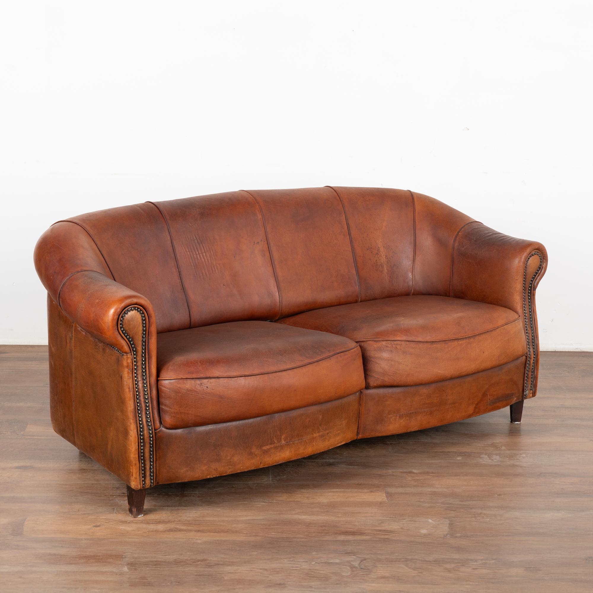 Vintage leather has an appeal all its own, especially when worn and weathered as seen in this handsome two-seat sofa. The aged patina of the brown sheep's skin leather leather has deepened through generations of use.
The gently rolled arms have