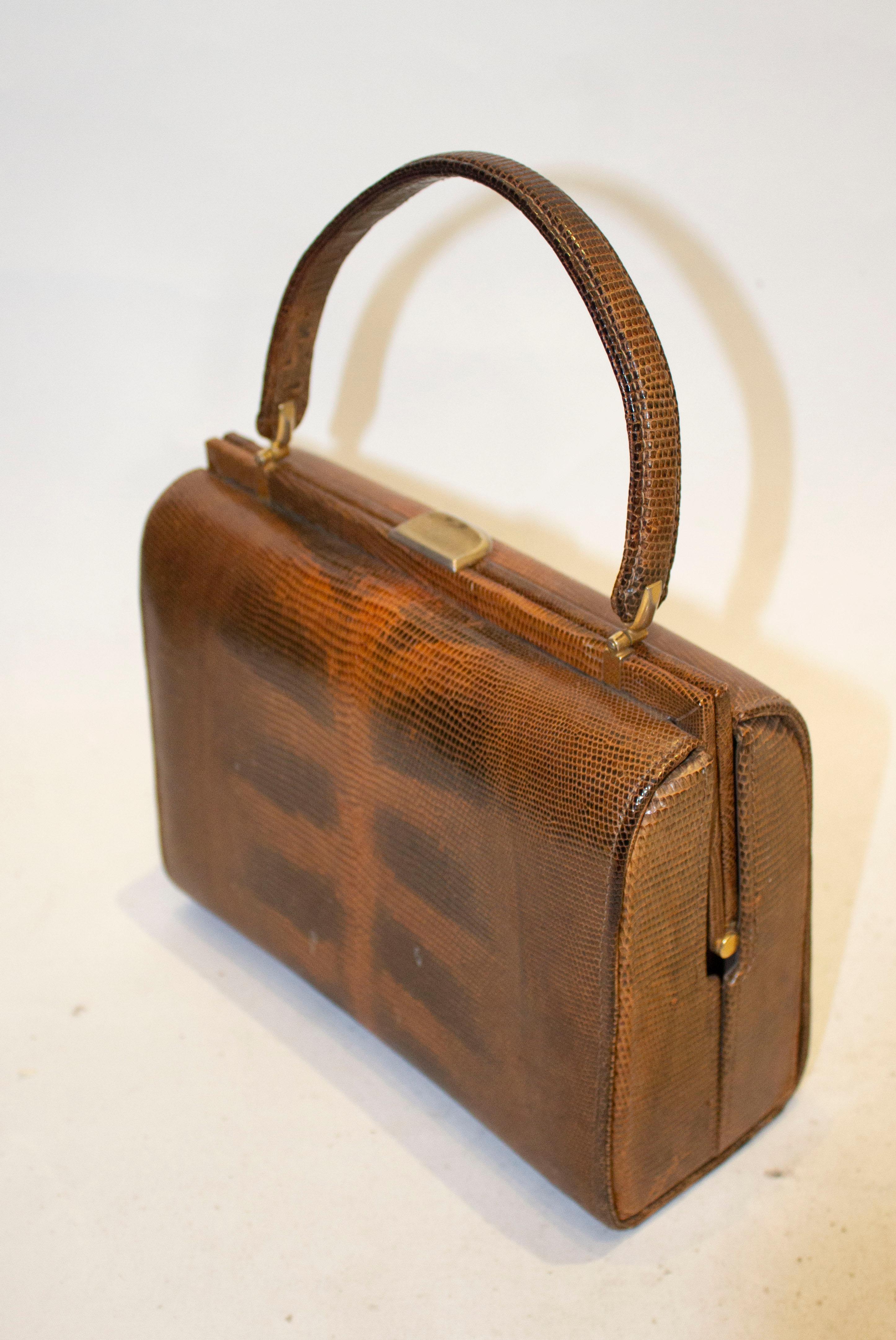 A vintage brown lizzard top handle hand bag.  The bag is lined in suede , and has one zip pocket,  one pouch pocket and a poppe pocket. 
Measurements: length 9''.width 4'' height ''