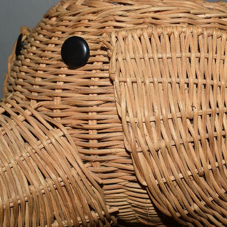 A whimsical brown wicker elephant basket that will be a wonderful addition to a nursery. This piece is created from wicker, with a trunk pointed up for good luck, and black button eyes. A small bamboo handle hangs from its mouth.